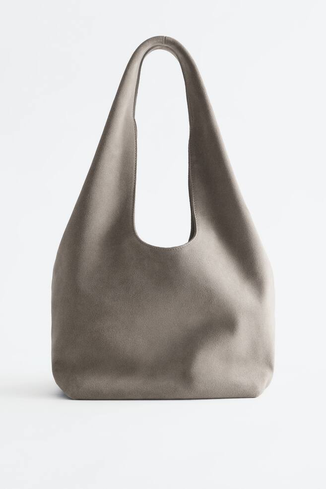 Un cabas en cuir suÃ©dÃ© fendu, dans une teinte gris taupe, est prÃ©sentÃ© debout, de face. Il met en valeur une silhouette souple et spacieuse, avec une large bandouliÃ¨re intÃ©grÃ©e et un fond plat. - 1