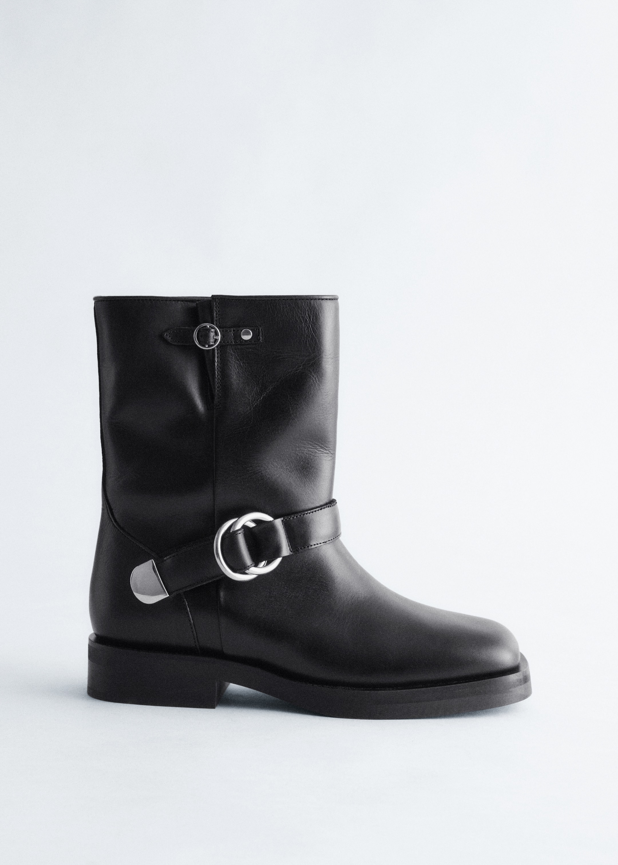 View larger image: The black leather boot is facing LEFT, featuring a mid-calf shaft and a chunky sole with a low block heel. It is adorned with a large silver-toned O-ring buckle strap around the ankle and a smaller silver-toned D-ring buckle strap near the top of the shaft.