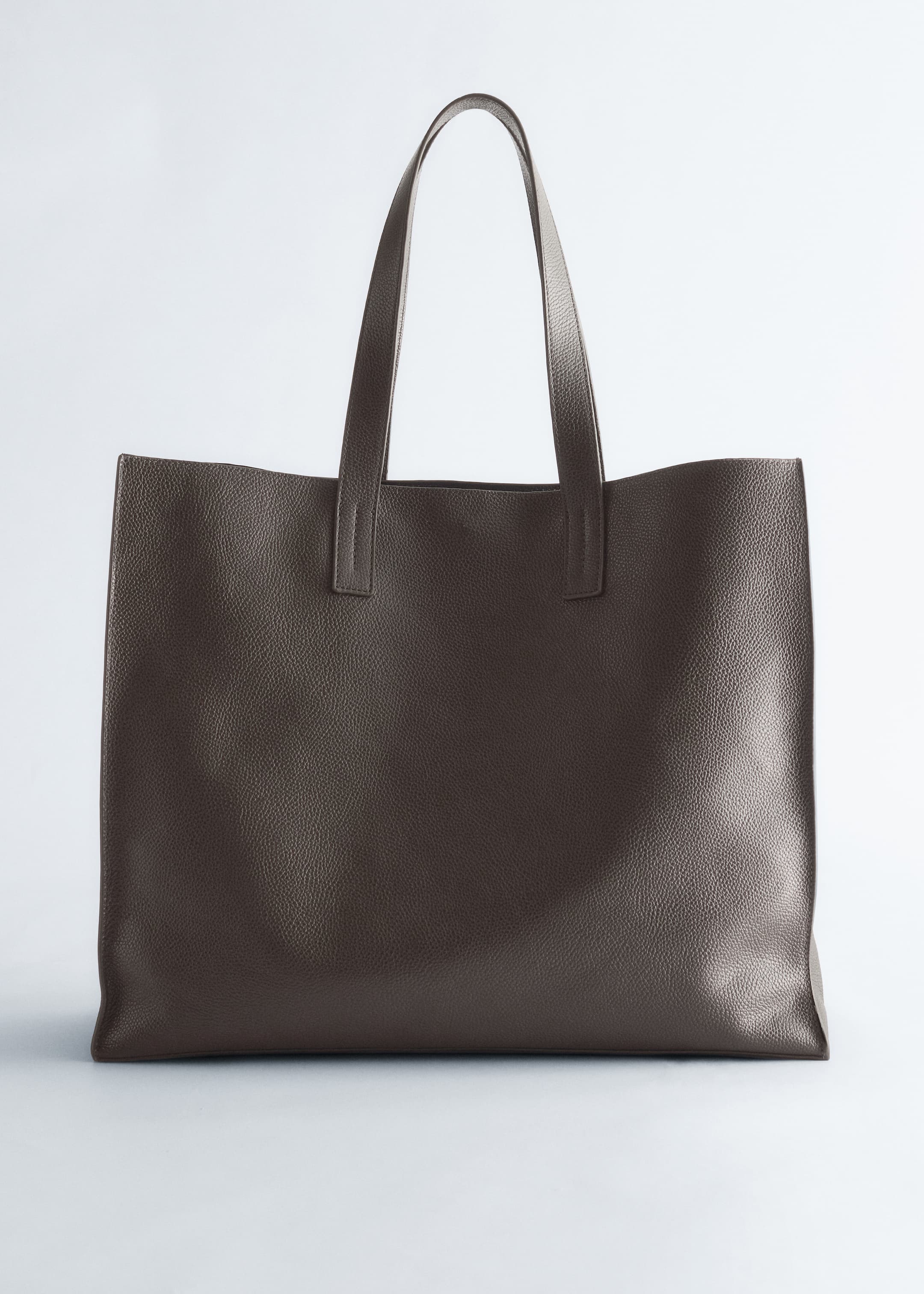 Ver imagen más grande: Un bolso tote de color topo oscuro está de pie, mirando al frente. El bolso rectangular presenta una textura granulada y dos correas de hombro planas que están unidas a su borde superior.