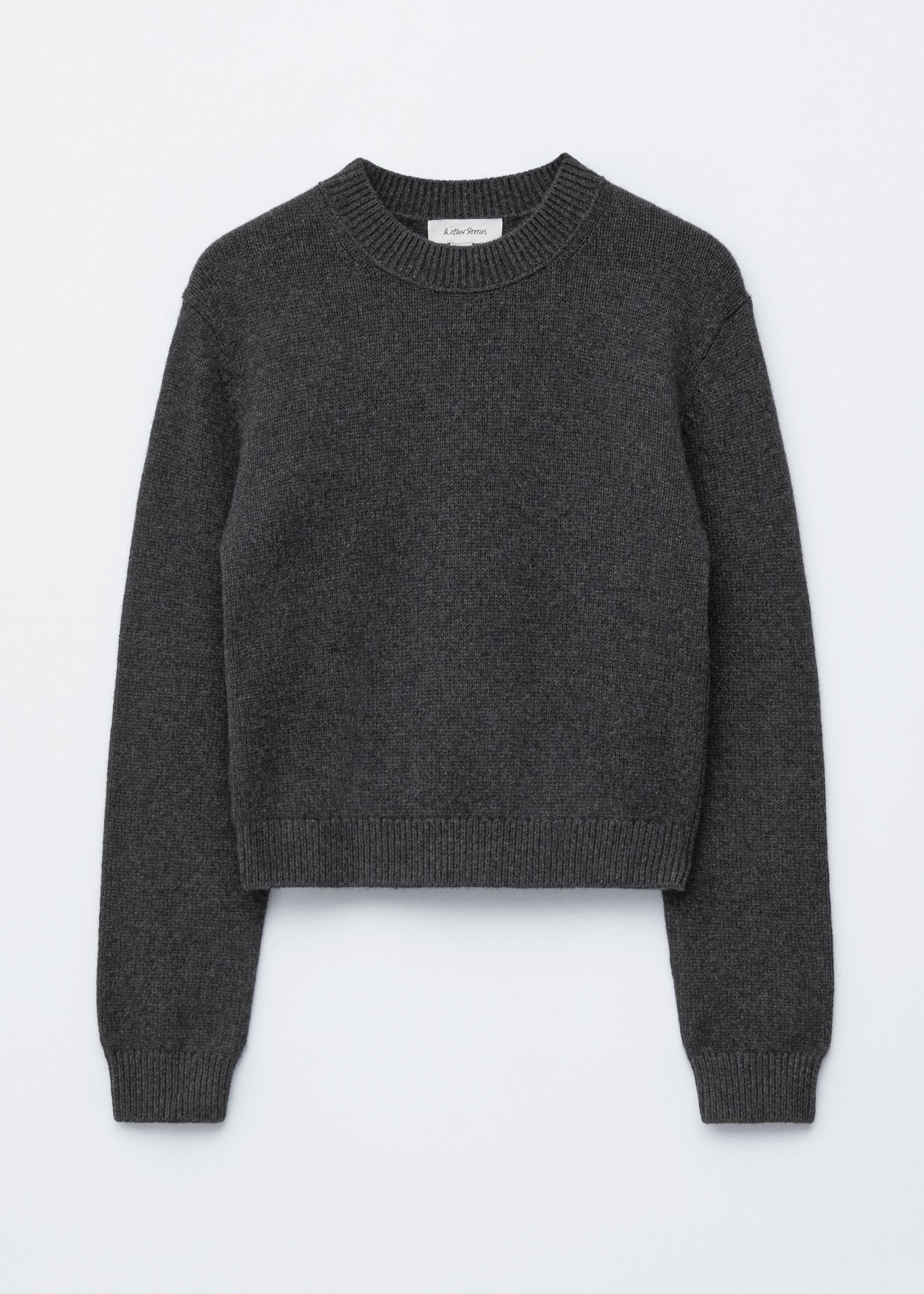 Größeres Bild ansehen: Ein dunkelgrauer Strickpullover ist von vorne sichtbar, mit einem gerippten Rundhalsausschnitt und sanft fallenden Schultern. Er zeigt lange Ärmel mit gerippten Bündchen und einem gerippten Saum, die in einer schlanken und kurzen Passform erscheinen.