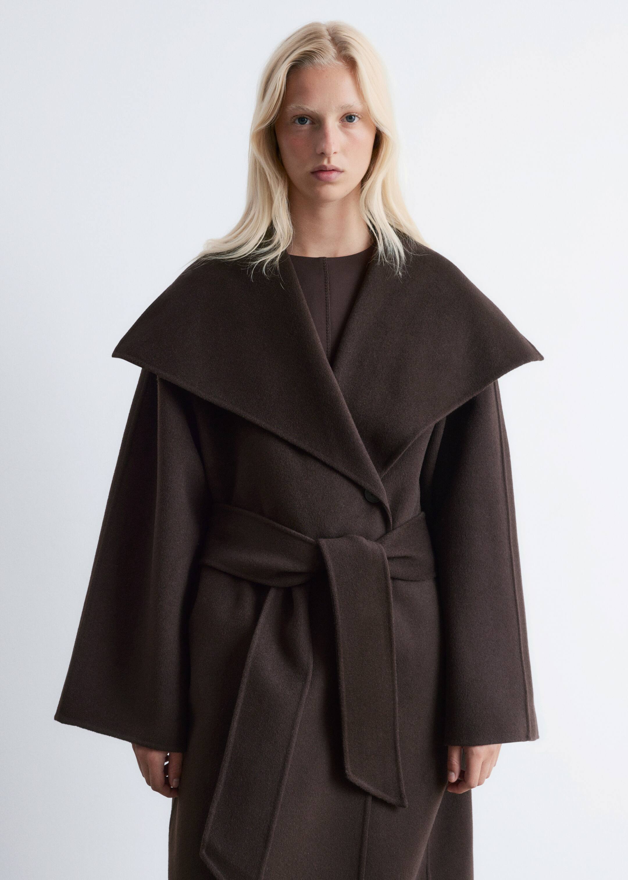 Visualizza immagine più grande: Un cappotto avvolgente marrone scuro è indossato frontalmente, caratterizzato da ampi revers a scialle e una cintura in tessuto annodata in vita. Il cappotto presenta una vestibilità rilassata con maniche ampie, e un indumento marrone è visibile sotto.