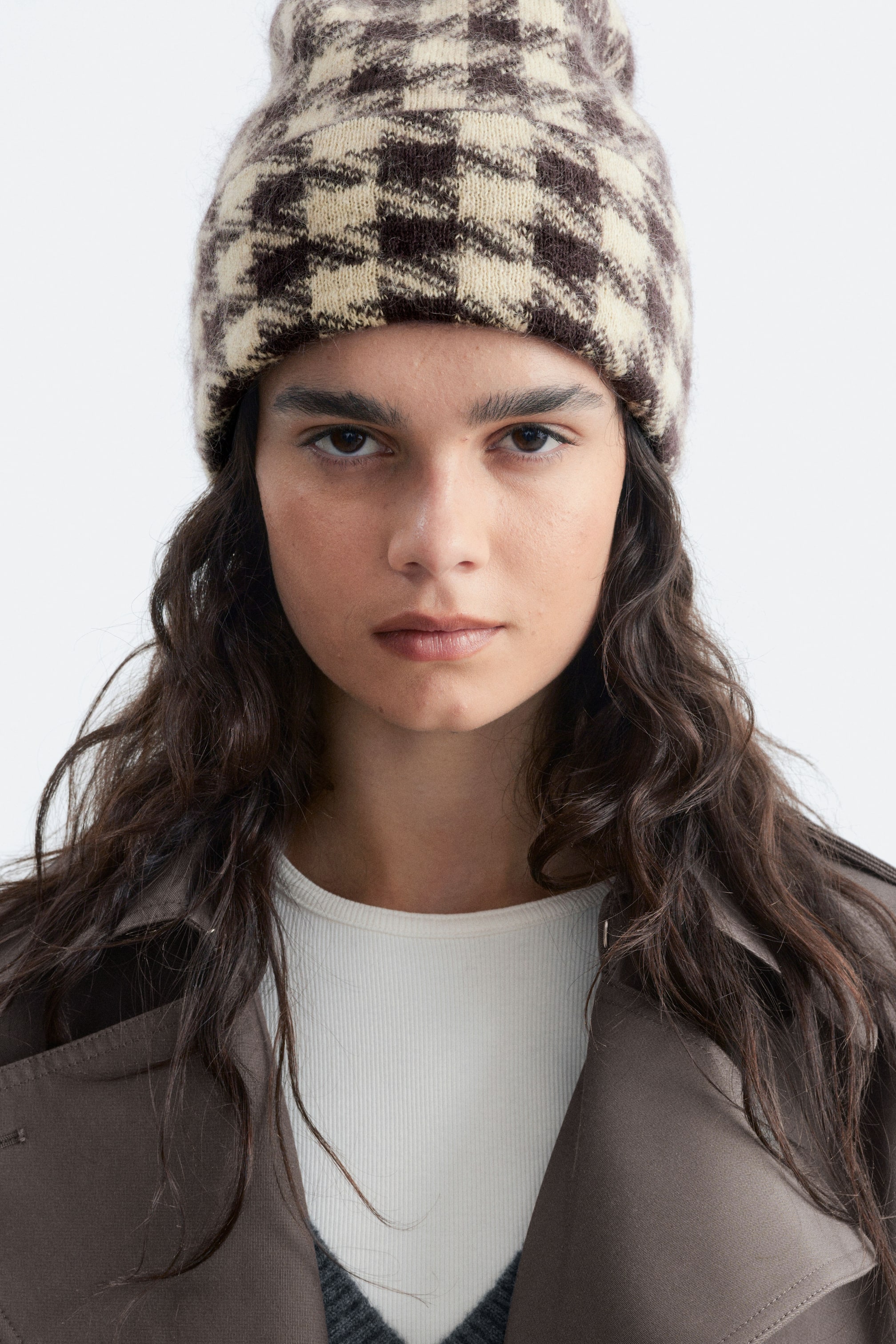 Agrandir l'image: Un bonnet à carreaux marron et crème, doté d’une texture tricotée duveteuse et d’un revers replié, est porté par le modèle.