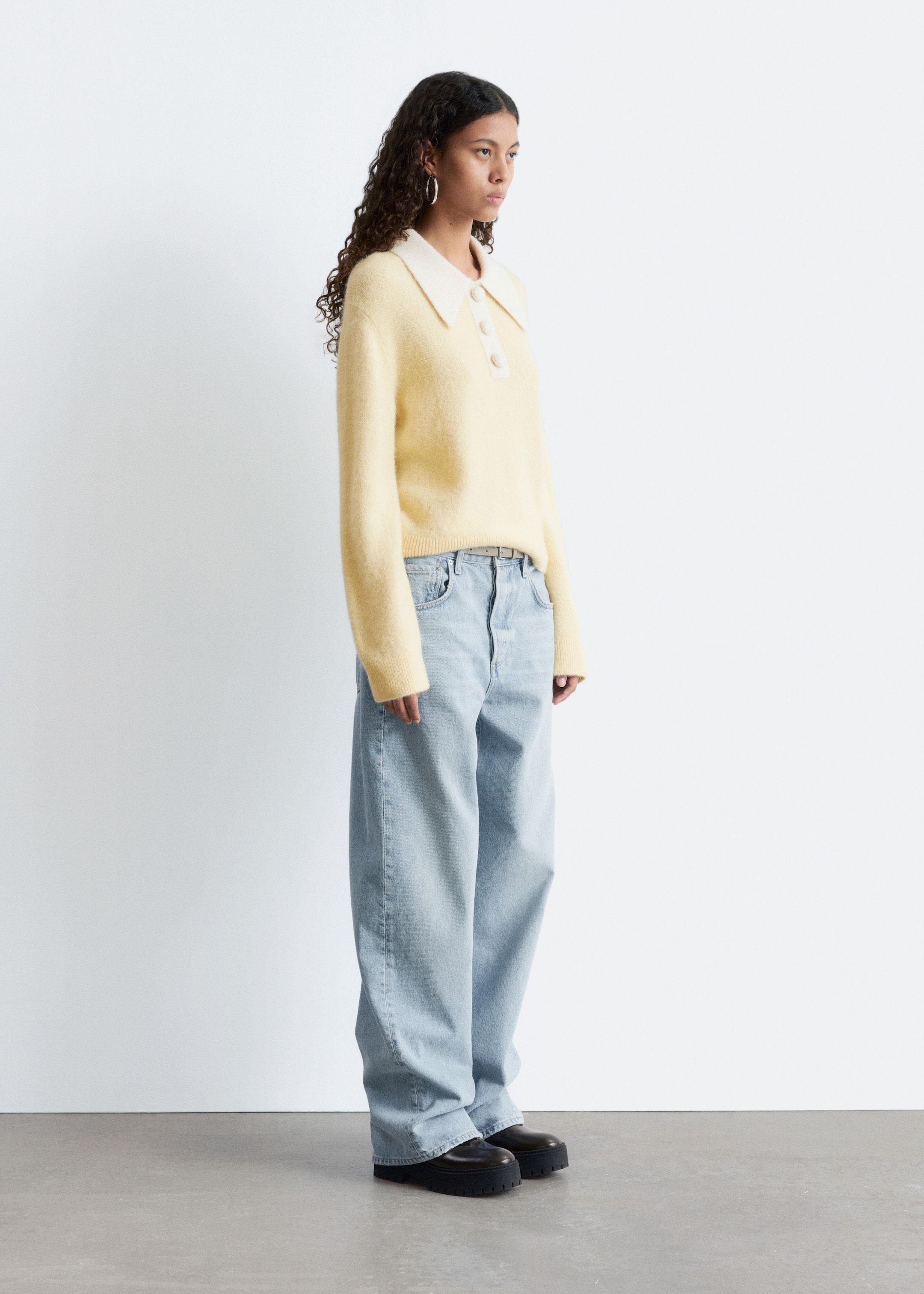 View larger image: A light yellow, fuzzy-textured polo sweater is being presented in a side view, featuring a cream collar and a three-button placket. The sweater is showcasing long sleeves and a relaxed fit, and is being styled with light wash, wide-leg jeans that are pooling over black, chunky-soled shoes.