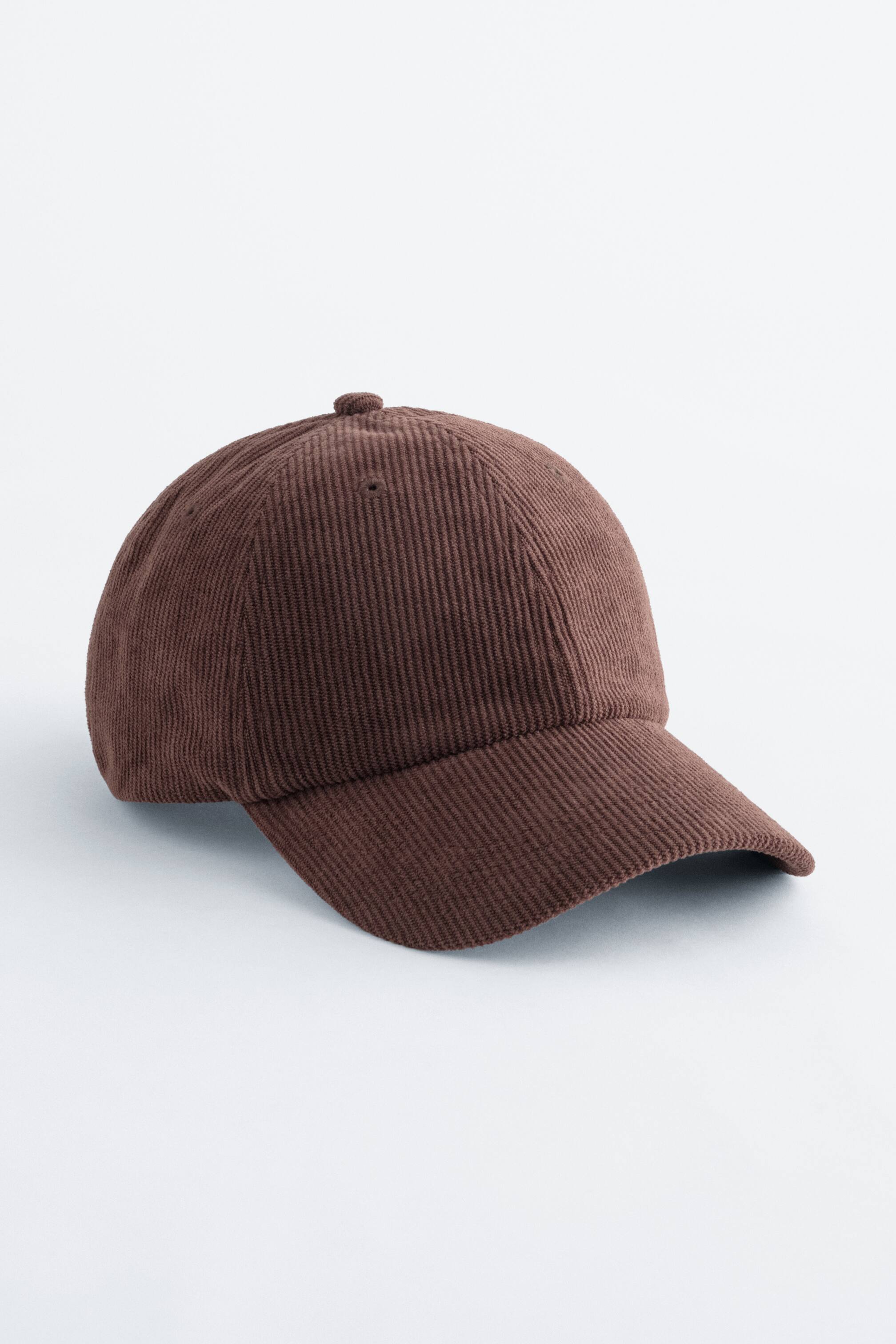 Agrandir l'image: Une casquette de baseball en velours côtelé marron est orientée vers l'avant, mettant en valeur son tissu texturé avec des côtes verticales. Elle présente une visière incurvée, un bouton sur le dessus et des œillets de ventilation sur la calotte.