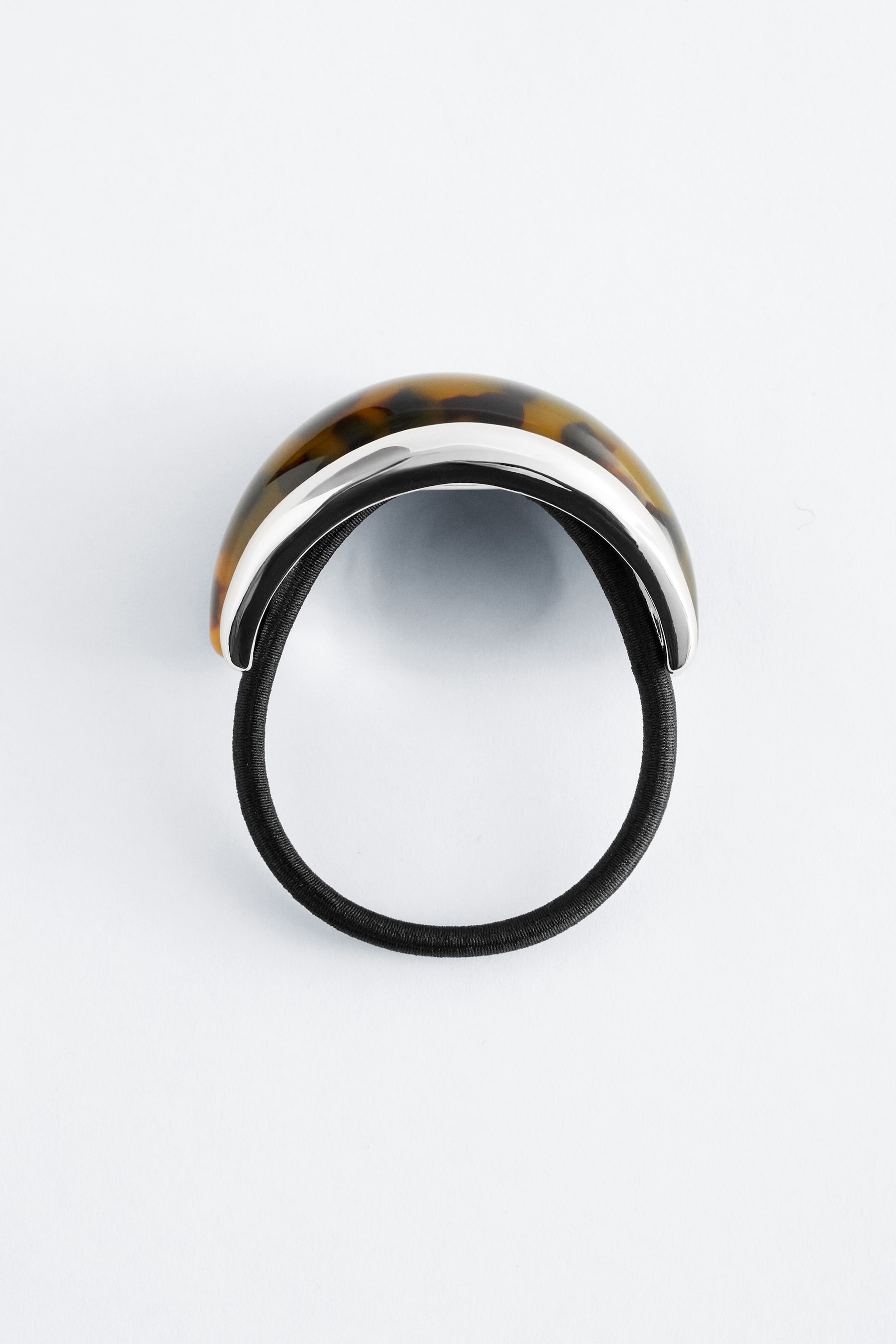 Grotere afbeelding bekijken: Een elastische haarelastiek presenteert een zwarte elastische lus, met een gebogen, koepelvormig decoratief element bovenop. Het element heeft een zilverkleurige metalen basis en een schildpadpatroon.