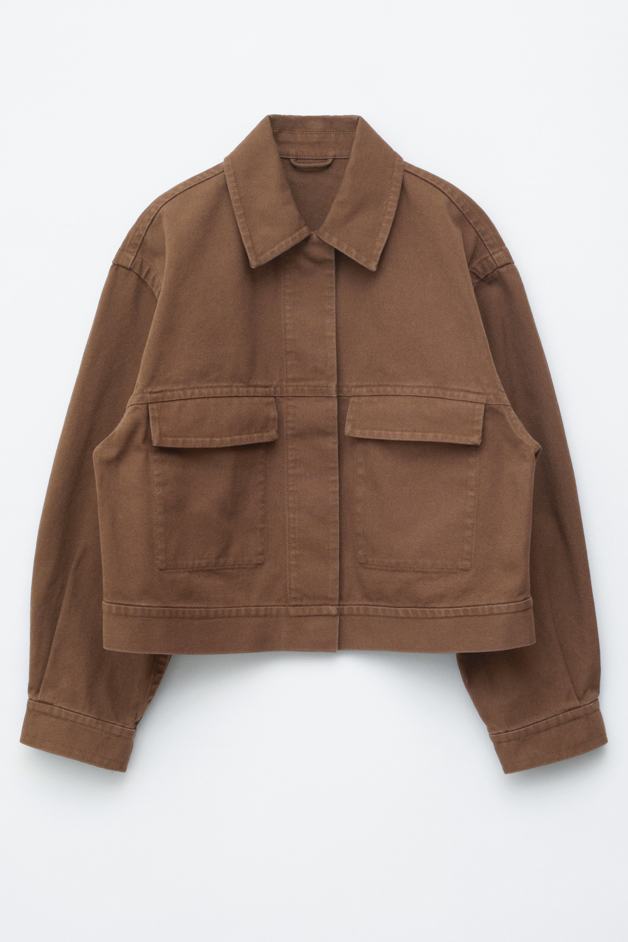 Se større billede: Den brune jakke vises forfra og har en boxy silhuet, en spids krave, to store flaplommer foran, en skjult knapstolpe og synlige skæresømme.