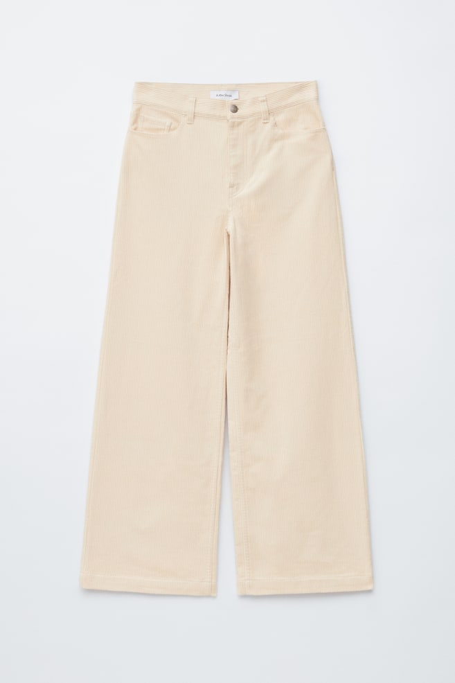 The light beige corduroy wide-leg pants are showcasing their front design, featuring a button and zip closure at the waist and two front slash pockets. - 1