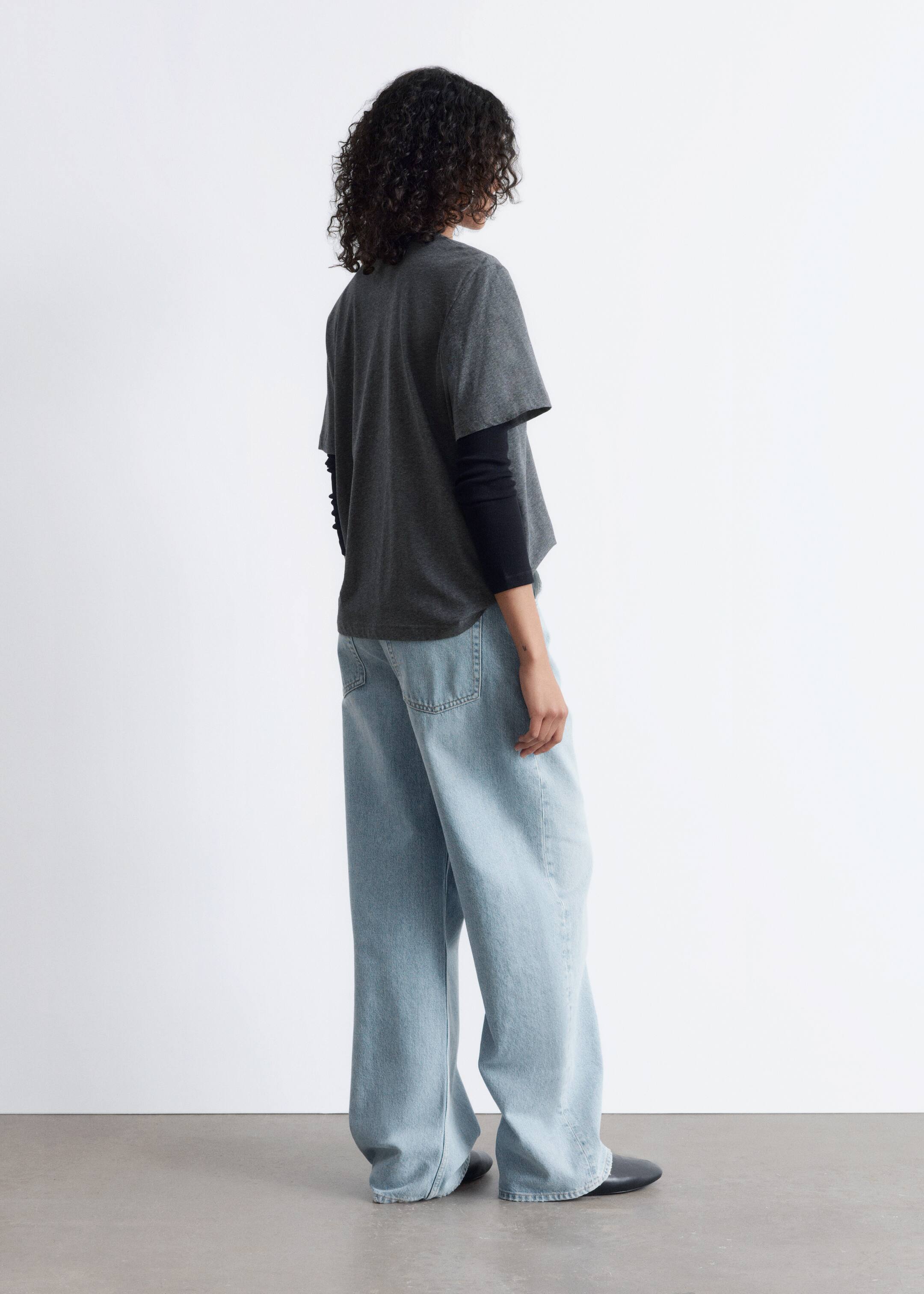 Vezi imaginea mai mare: Un tricou gri închis, lejer, este purtat peste un tricou negru cu mâneci lungi, asortat cu blugi largi, de culoare albastru deschis, văzuți dintr-un unghi posterior. Blugii au buzunare din spate vizibile și o croială largă.