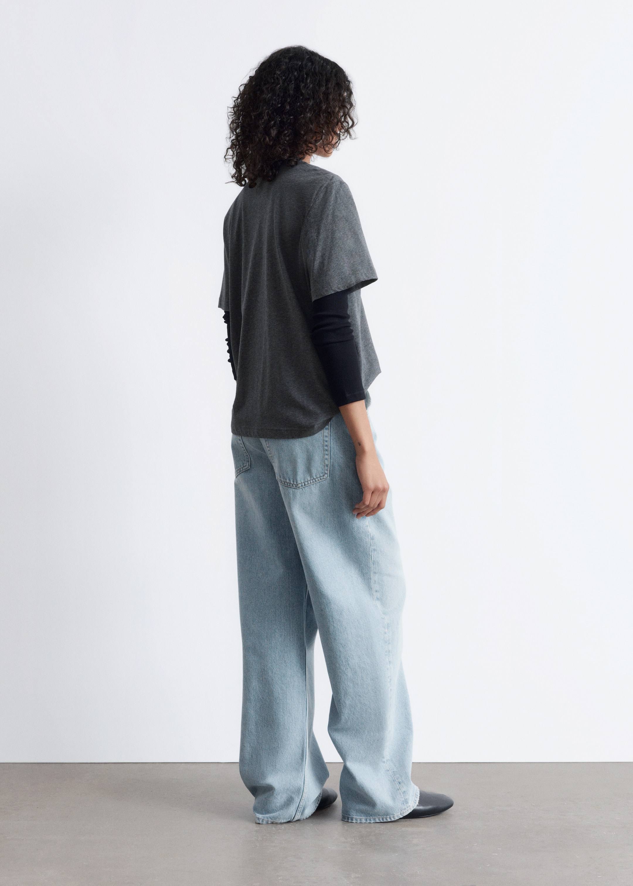 Grösseres Bild ansehen: Ein dunkelgraues, locker sitzendes T-Shirt wird über einem schwarzen Langarmhemd getragen und mit hellblauen, weit geschnittenen Jeans kombiniert, die aus einem Winkel von hinten betrachtet werden. Die Jeans haben sichtbare Gesäßtaschen und einen weit geschnittenen Bein.