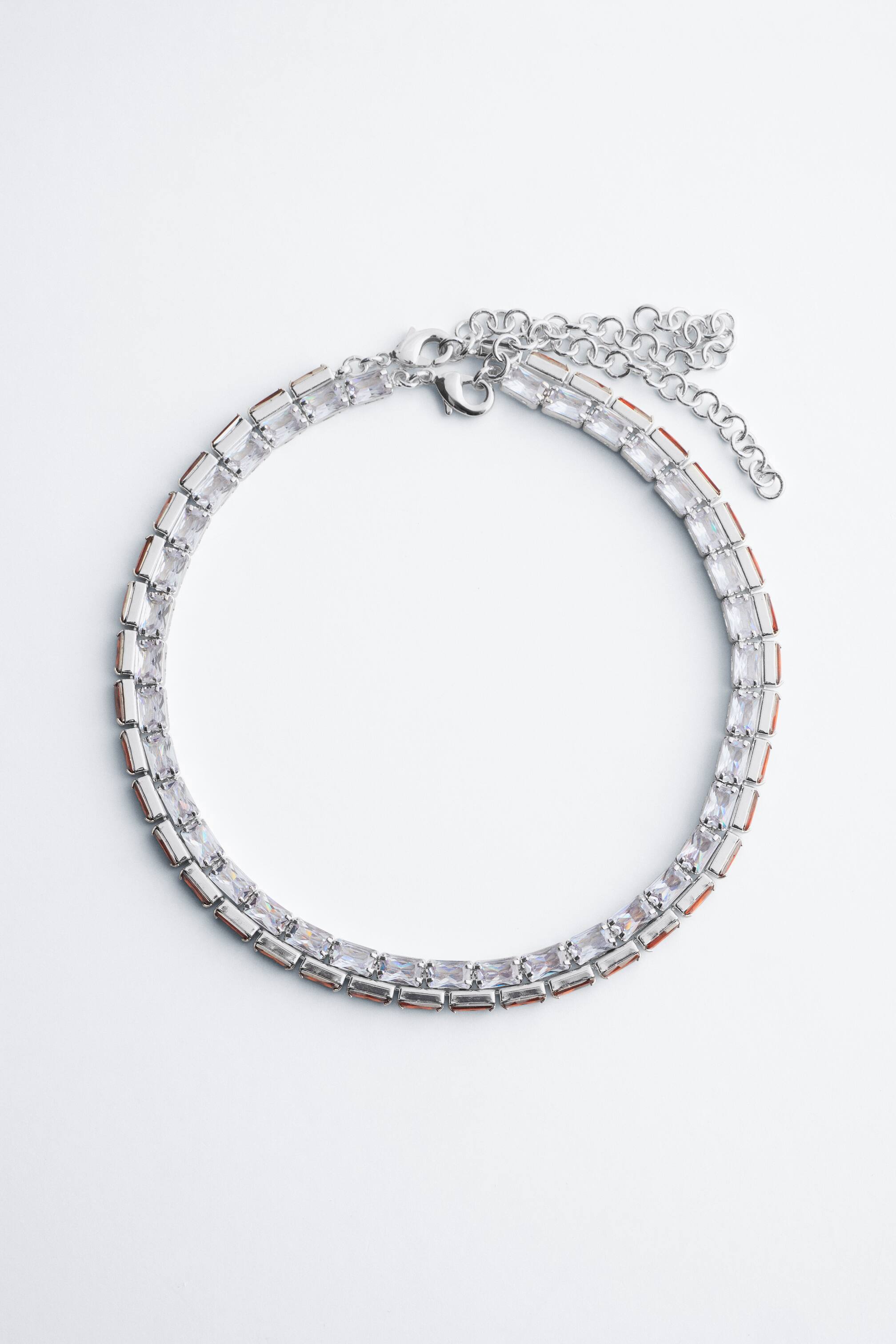View larger image: A silver-toned choker necklace lies flat in a circular shape, displaying closely set, rectangular-cut cubic zirconia stones. The necklace features a lobster clasp closure with an adjustable extension chain.
