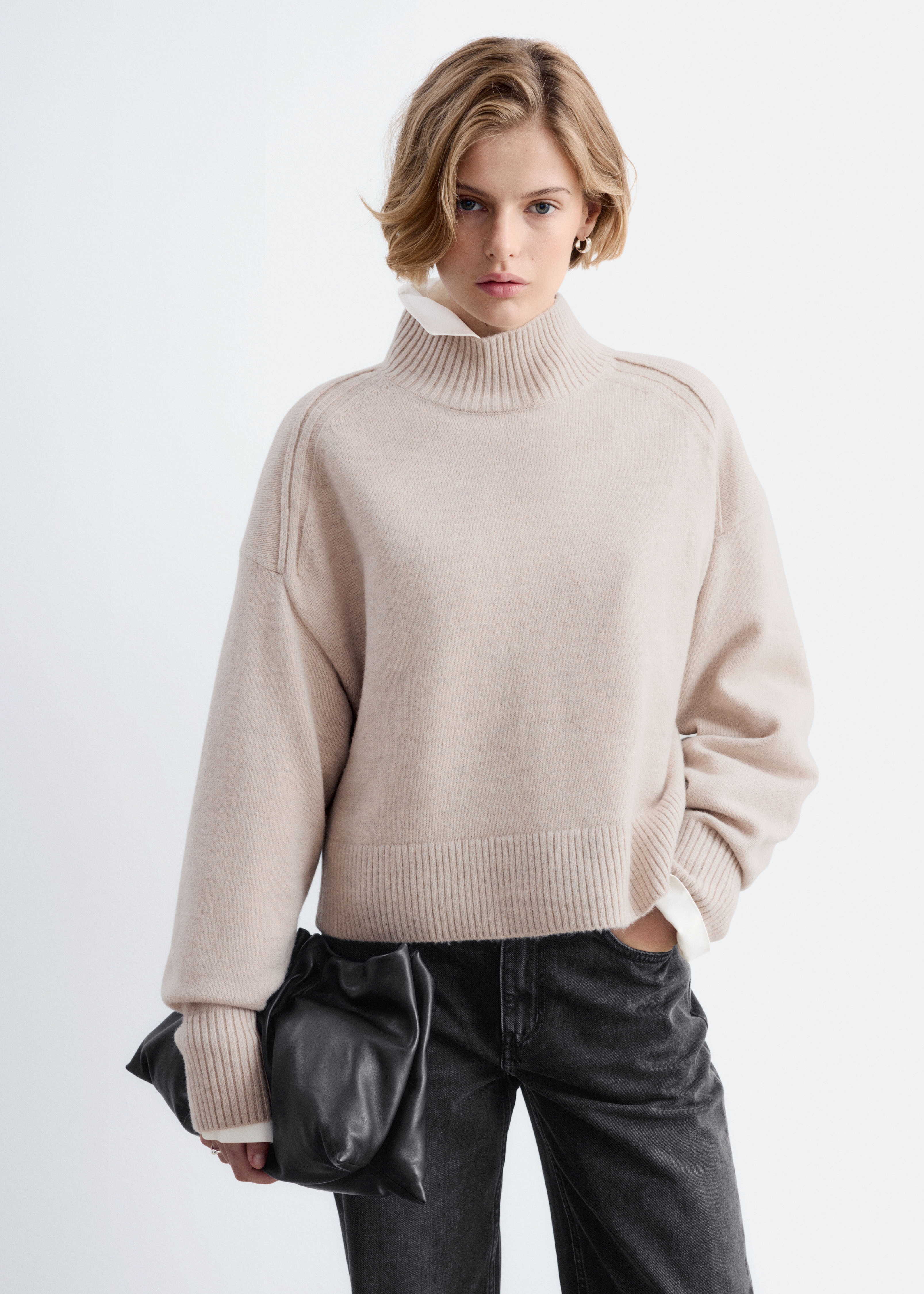 Un pulover bej cu guler Ã®nalt tip mock neck este prezentat din faÈÄ, evidenÈiind o siluetÄ relaxatÄ, cu cusÄturi ale umerilor orientate spre faÈÄ. Este prevÄzut cu guler striat, tiv lat striat Èi mÃ¢neci lungi cu manÈete striate prelungite.