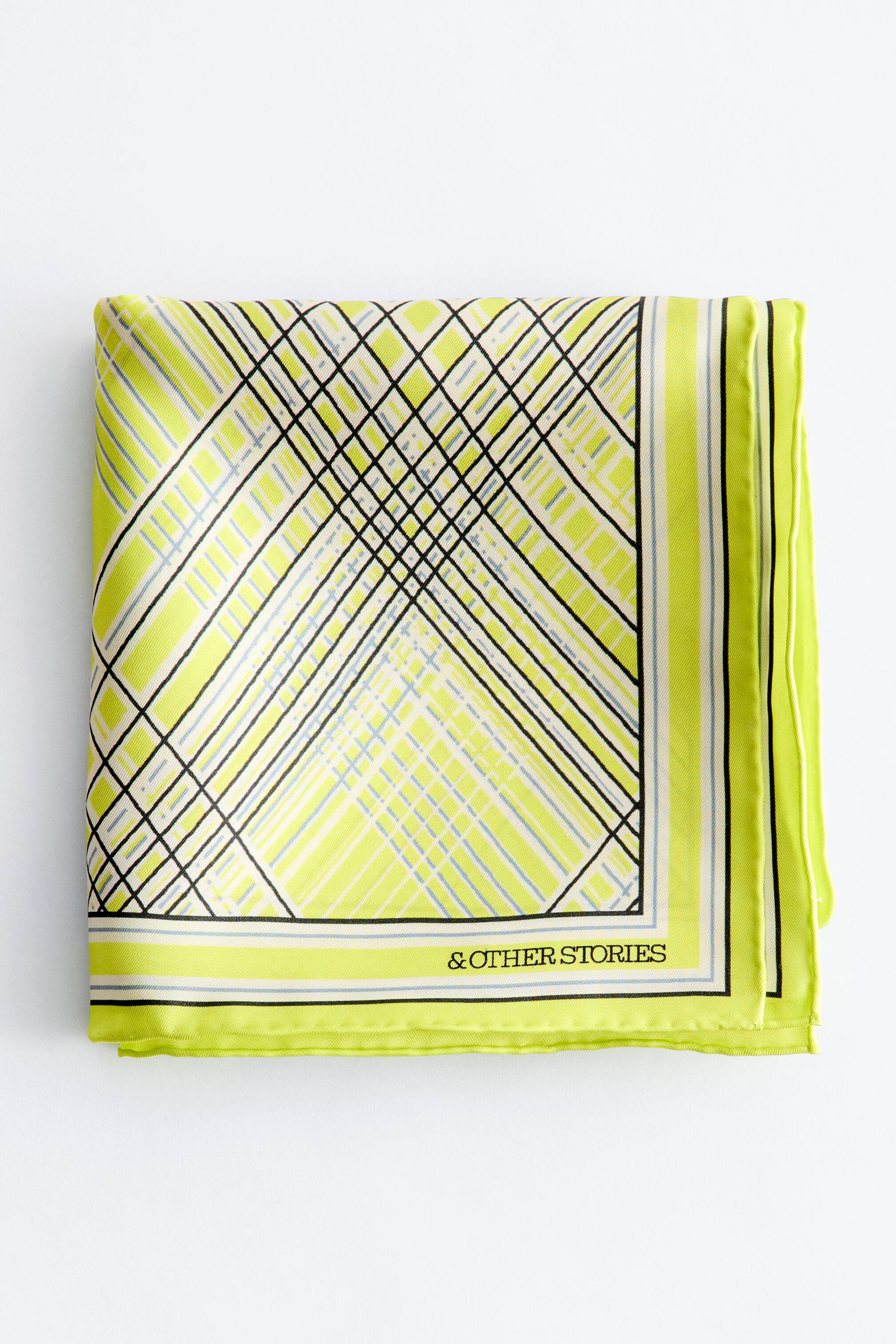 Größeres Bild anzeigen: Bedrucktes Seidentuch. Es ist zu einem Quadrat gefaltet und zeigt ein geometrisches Muster aus sich kreuzenden schwarzen und hellblauen diagonalen Linien über limettengrünen und cremeweißen Streifen. Ein markanter Rand, der limettengrüne, schwarze und cremeweiße Streifen aufweist, umrahmt das Design, wobei "& OTHER STORIES" unten rechts sichtbar ist.