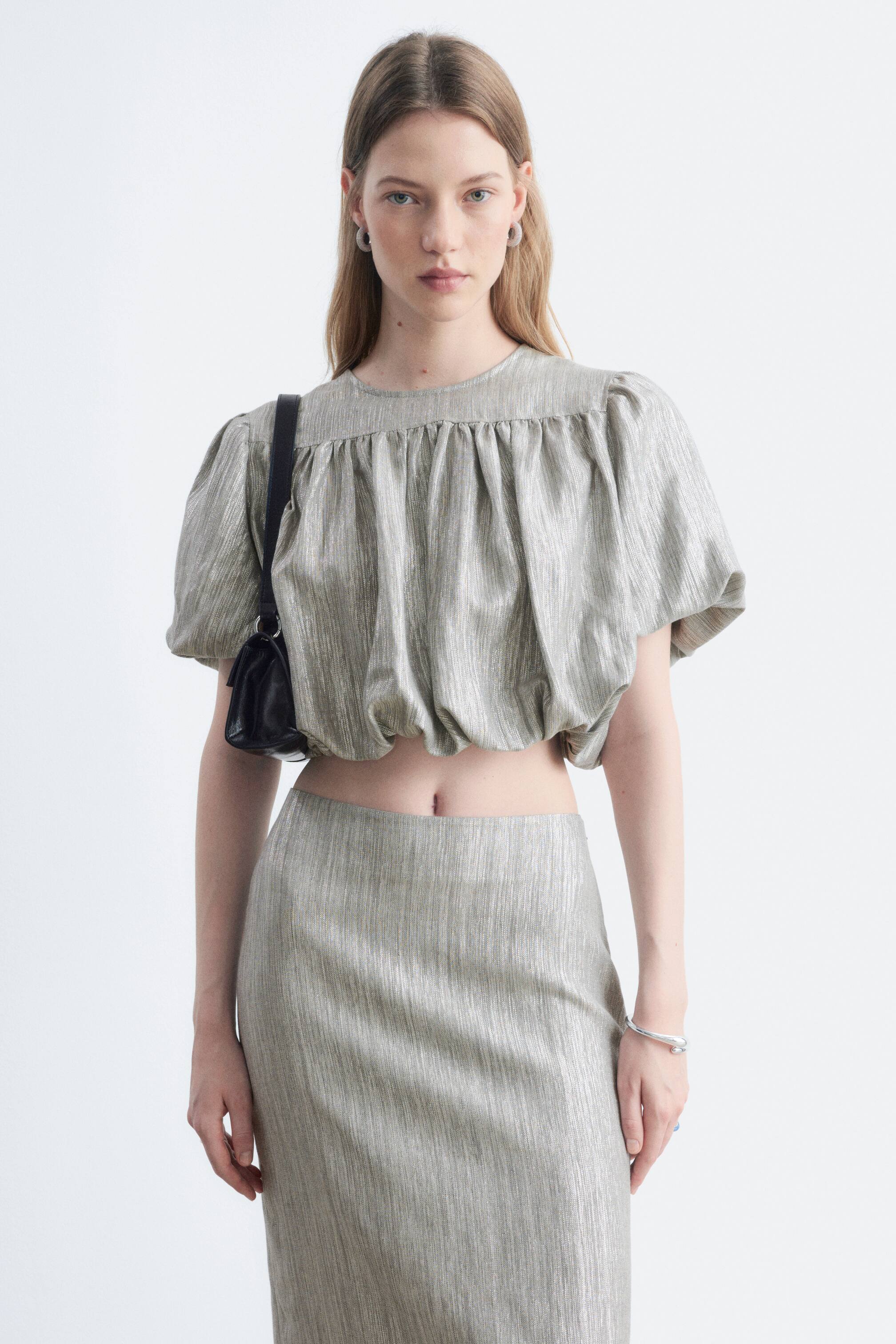 View larger image: A shimmering two-piece set featuring vertical textured stripes is shown. It consists of a cropped top with a round neckline, puffed short sleeves, and gathered fabric creating volume at the neckline and hem, alongside a matching straight midi skirt worn high-waisted.