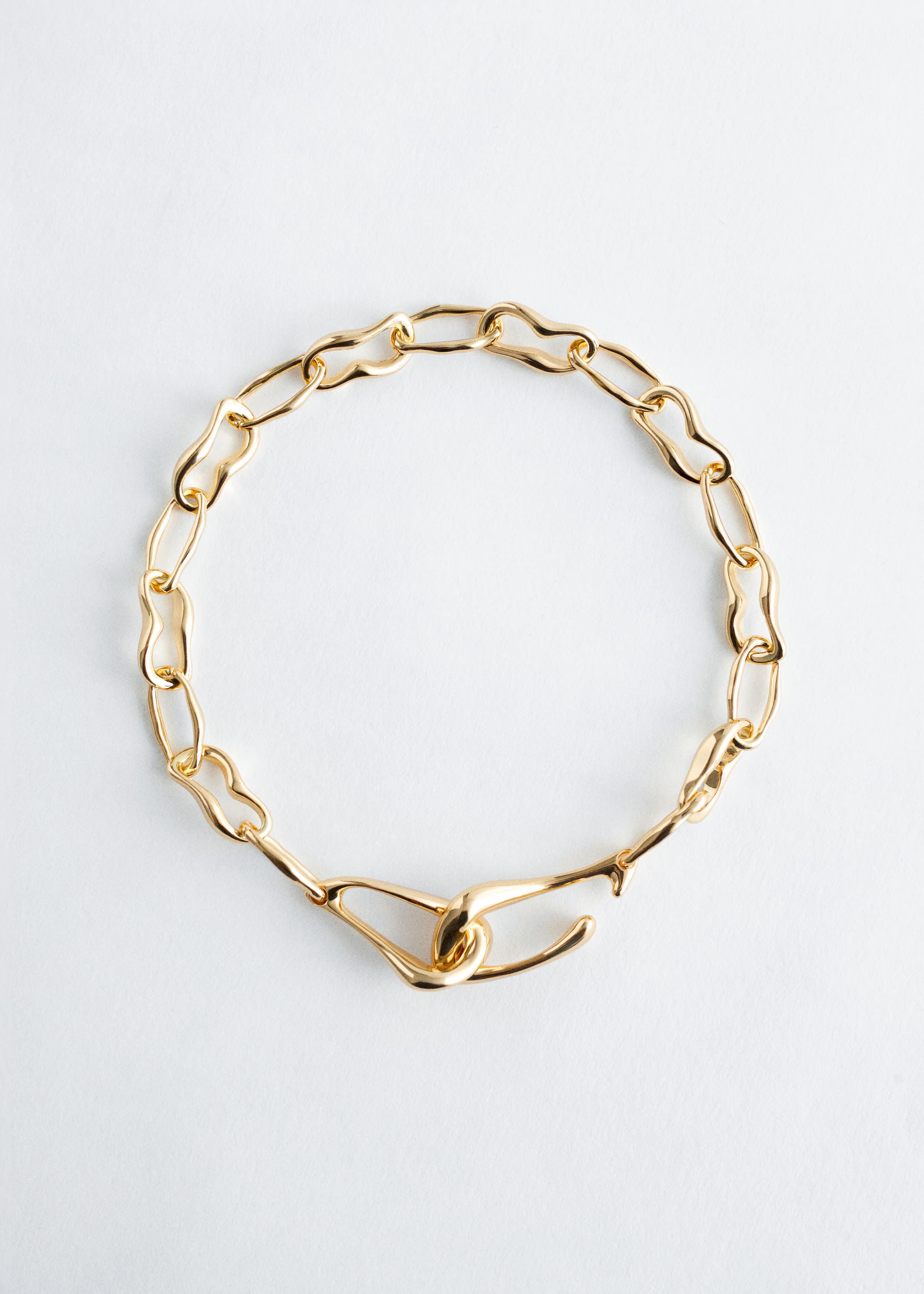 View larger image: A gold-toned necklace is featuring irregular, elongated links. An oversized hook clasp is connecting the ends at the front, functioning as both a fastener and a decorative element.