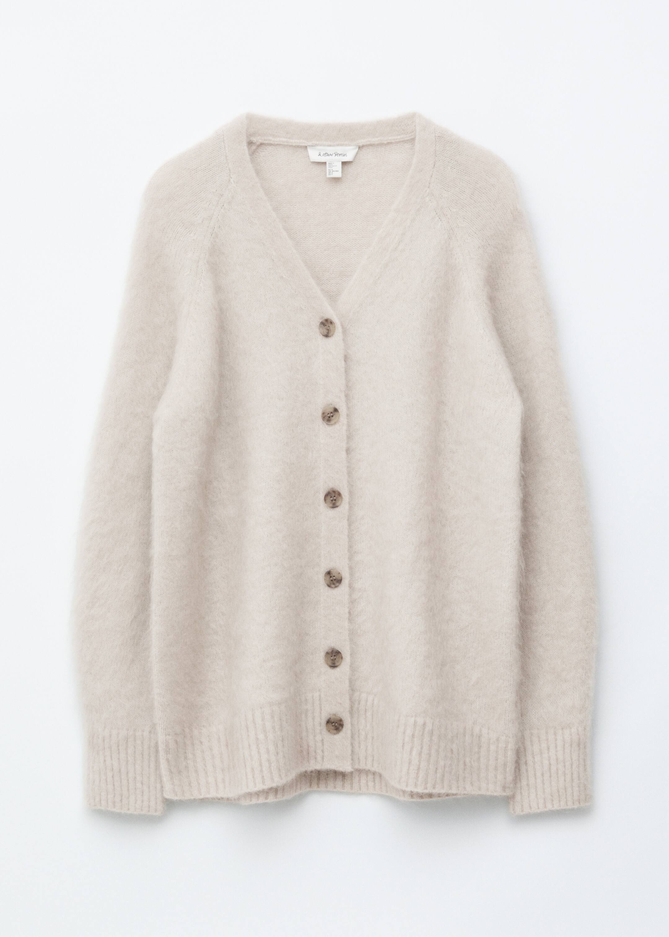 View larger image: A light beige cardigan is displaying its front, featuring a fuzzy knit texture, a V-neckline, raglan sleeves, and six round brown buttons down the center, finished with ribbed cuffs and hem.