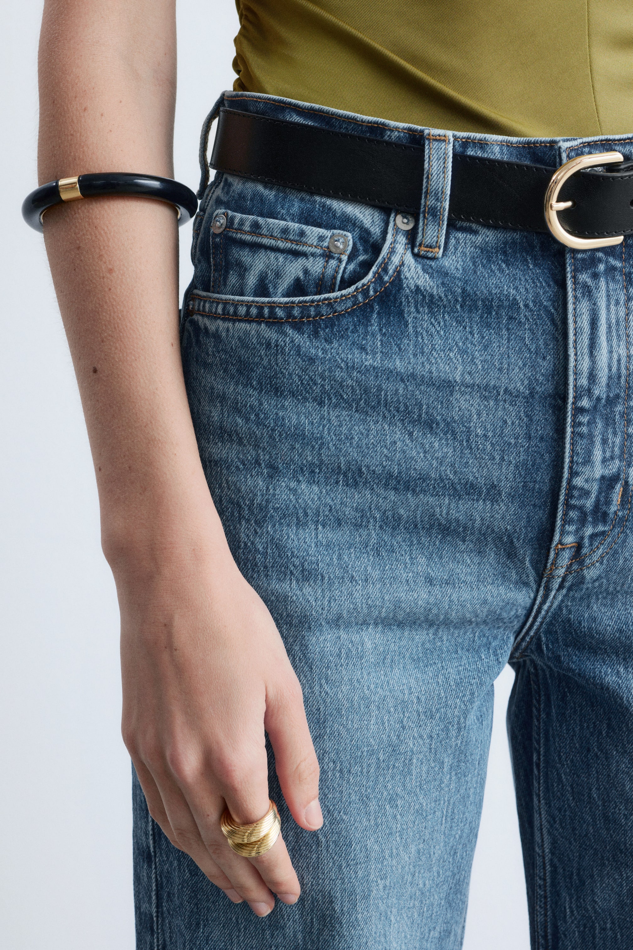 Grotere afbeelding bekijken: Een zwarte leren riem sluit blauwe denim jeans, met een goudkleurige afgeronde gesp.