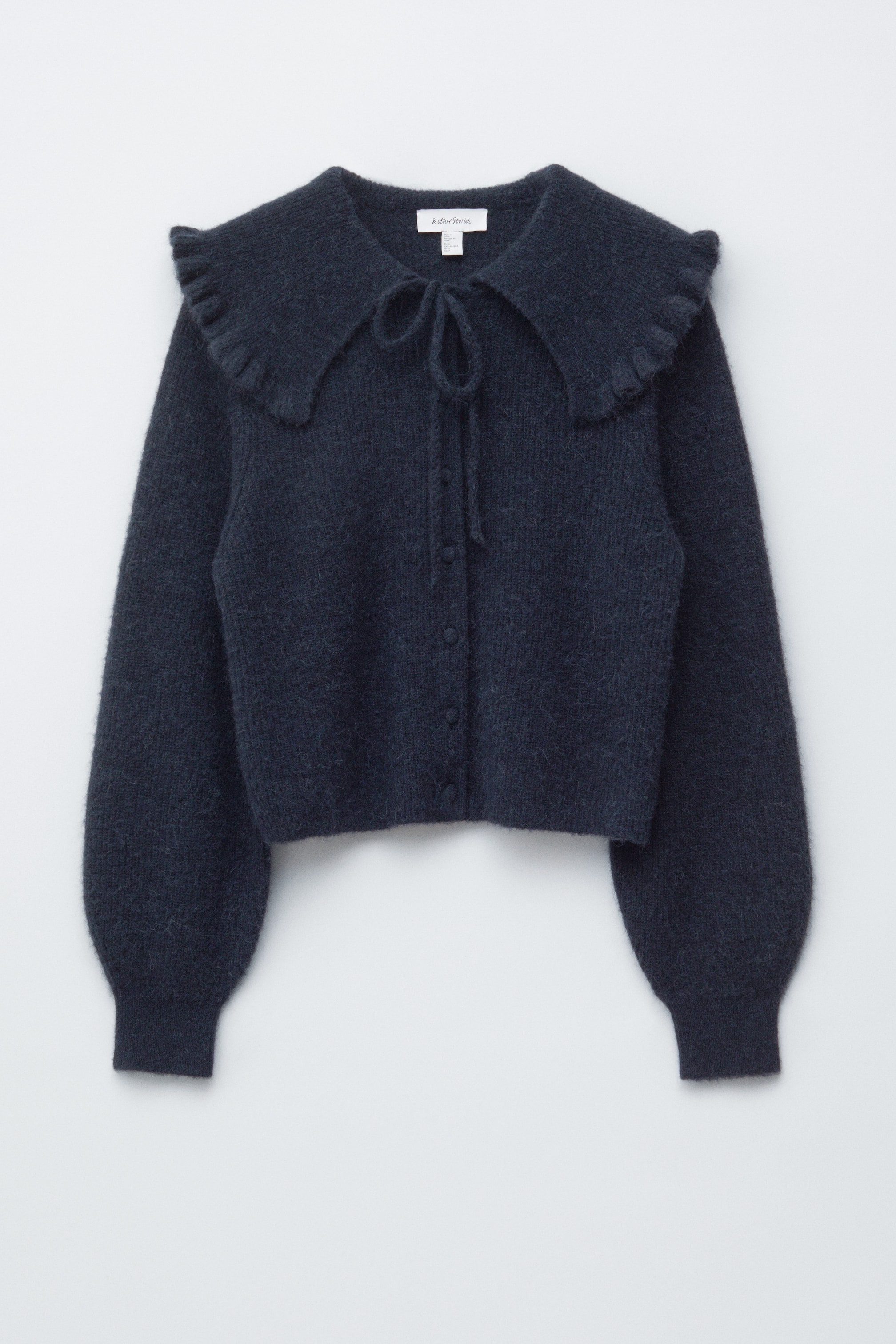 הצגת תמונה גדולה יותר: קרדיגן כחול כהה ומטושטש מוצג במבט קדמי, עם צווארון גדול ומקופל עם סגירת קשירה בקו הצוואר. הוא מעוצב עם כפתורים, והשרוולים הנפוחים שלו מתכנסים לתוך חפתים צמודים.