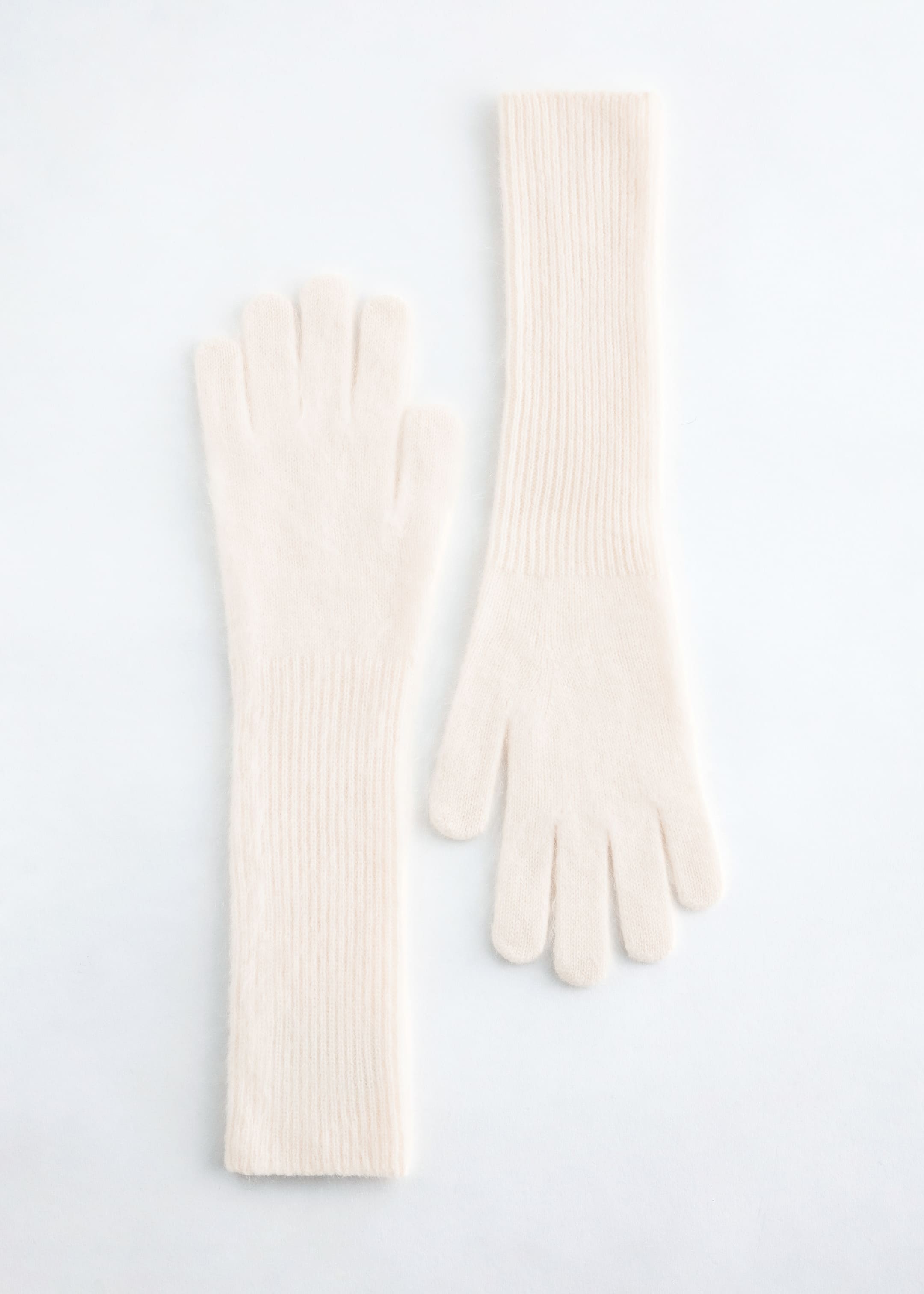 View larger image: Knitted brushed cashmere gloves are presenting their front sides, laid flat. They are cream-colored, featuring individual fingers and long, vertically ribbed cuffs extending past the wrist.