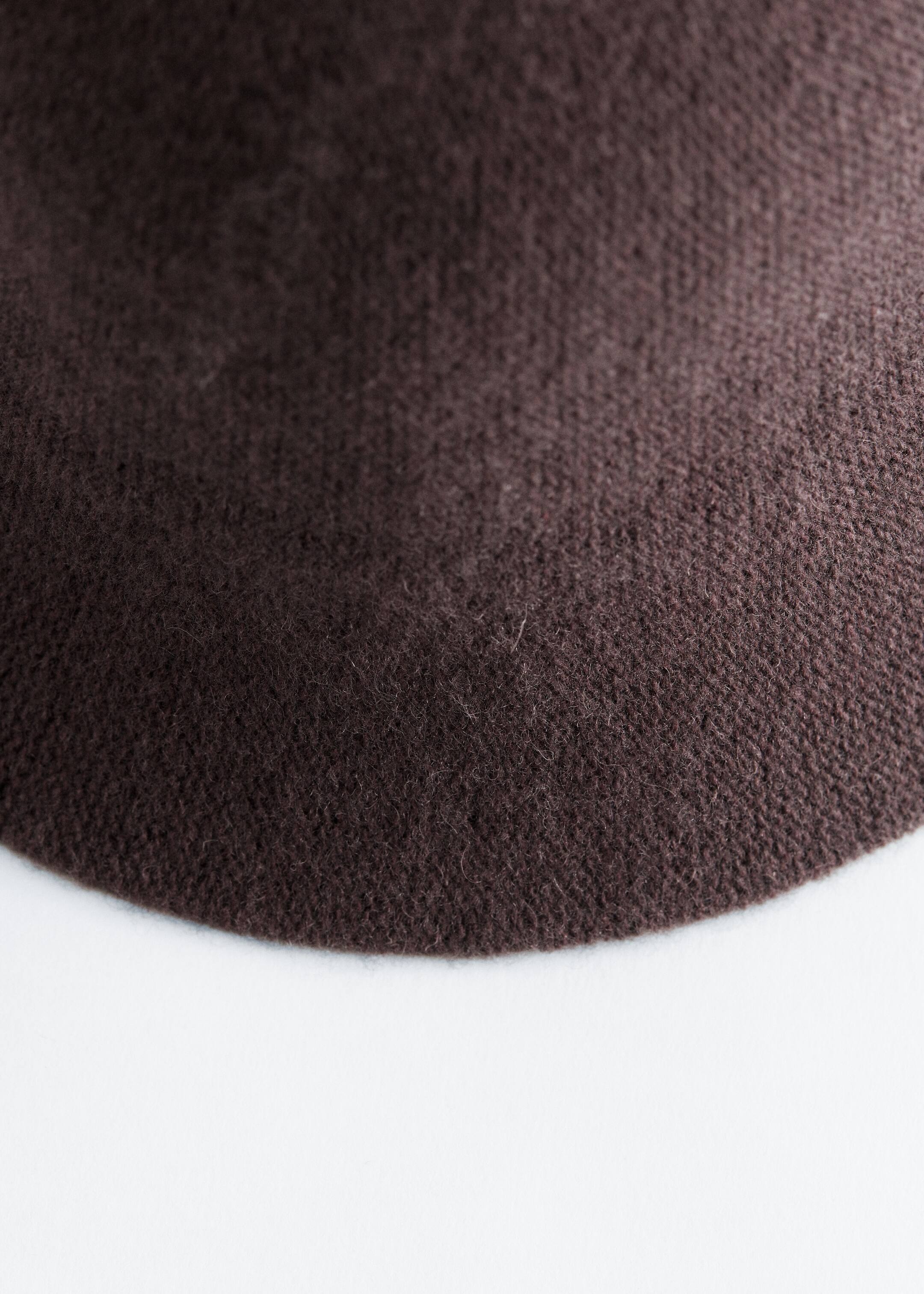 View larger image: The dark brown knitted wool blend fabric of a hat is showing a fine, soft texture. A curving edge is visible, indicating the hat's rounded shape.
