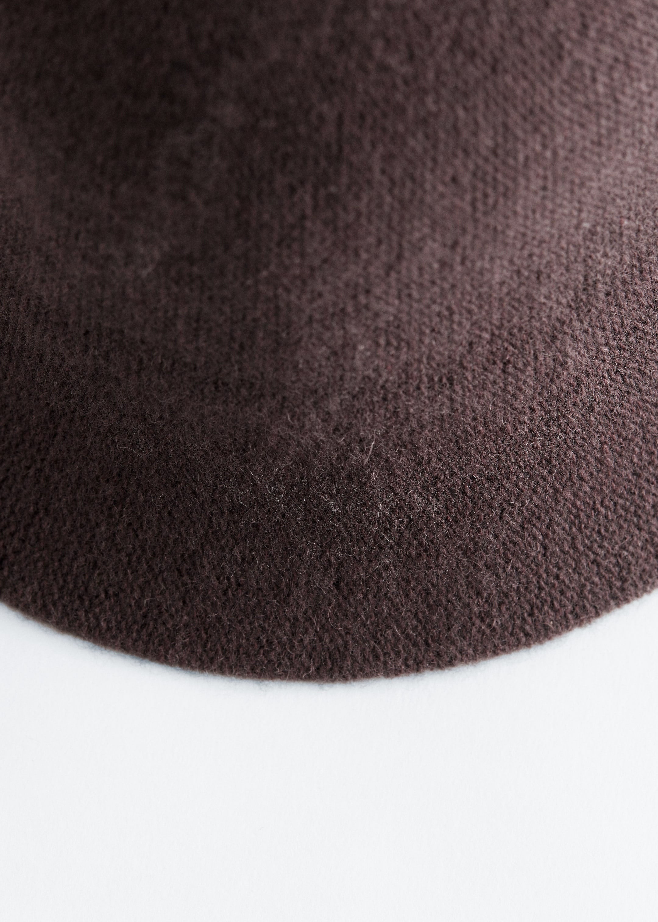 Agrandir l'image: Le tissu en laine mélangée tricotée brun foncé d'un chapeau présente une texture fine et douce. Un bord incurvé est visible, indiquant la forme arrondie du chapeau.