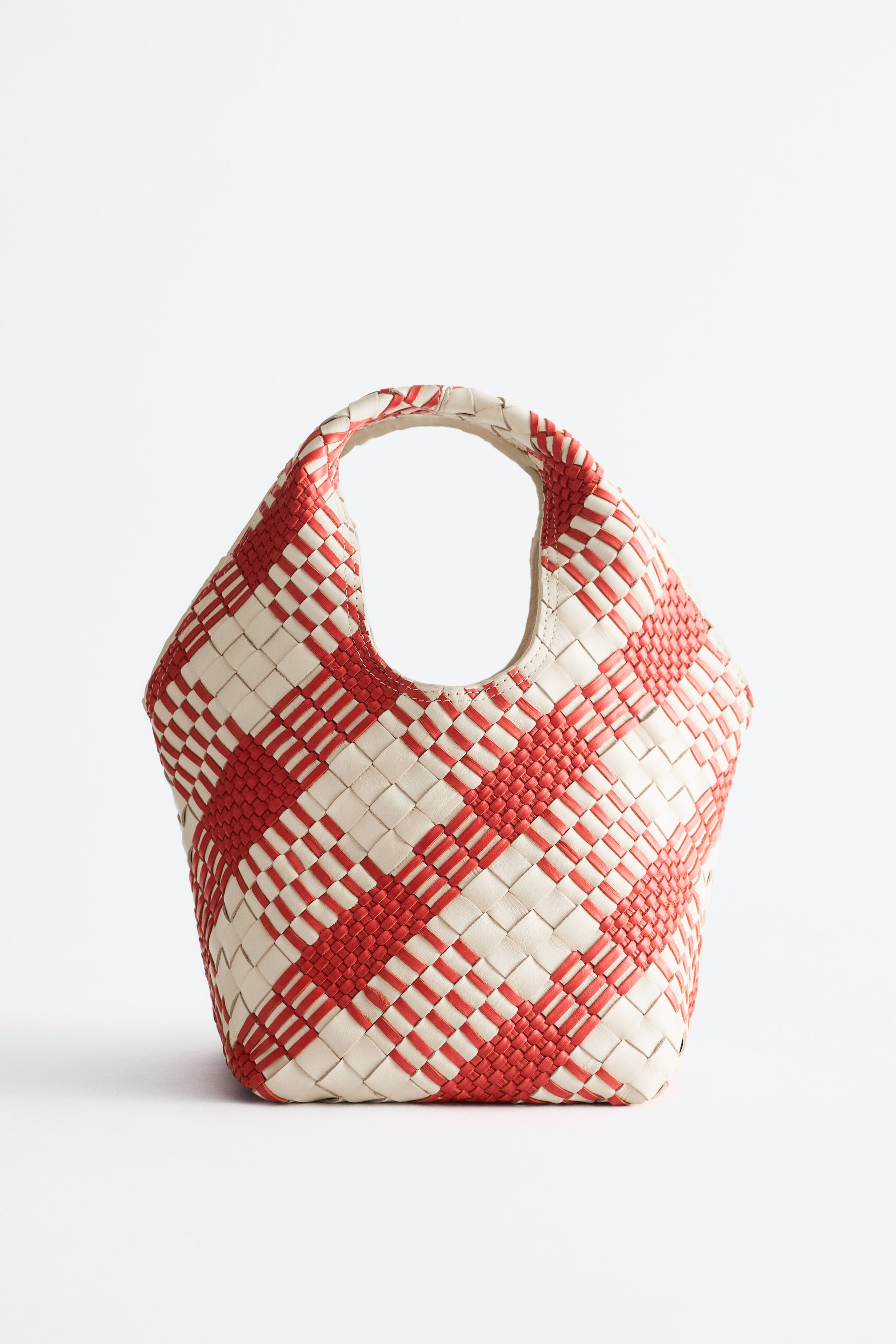 Προβολή μεγαλύτερης εικόνας: Μια τσάντα παρουσιάζεται από μπροστά, με χαλαρή σιλουέτα κατασκευασμένη από πλεκτό δέρμα σε ένα πλέγμα κόκκινου και υπόλευκου μοτίβου, με καμπυλωτό άνοιγμα στην κορυφή που σχηματίζει ενσωματωμένη λαβή.