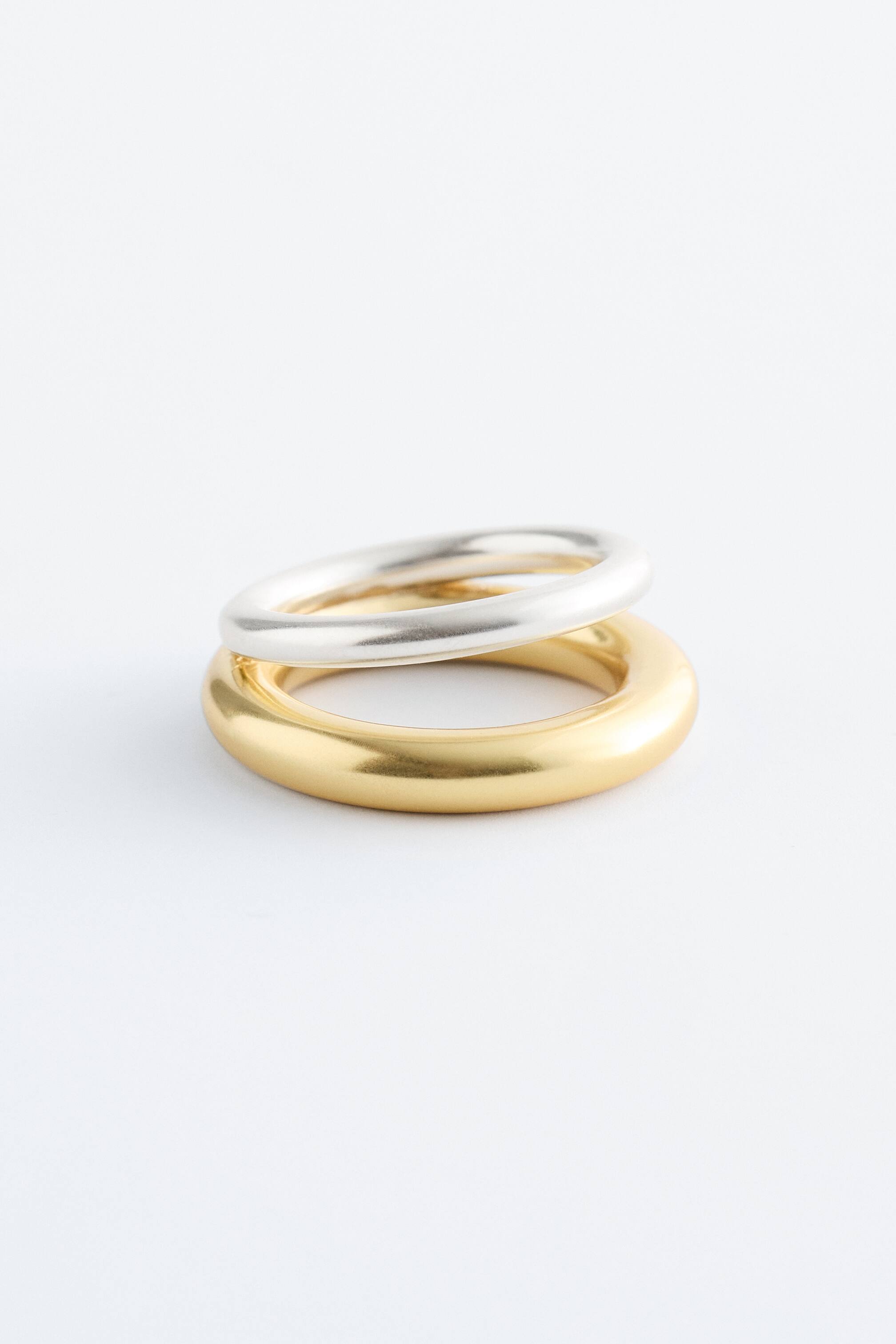Agrandir l'image: Deux bagues épaisses sont posées ensemble. Une bague de ton doré soutient une bague de ton argenté, et toutes deux présentent une finition lisse et mate.
