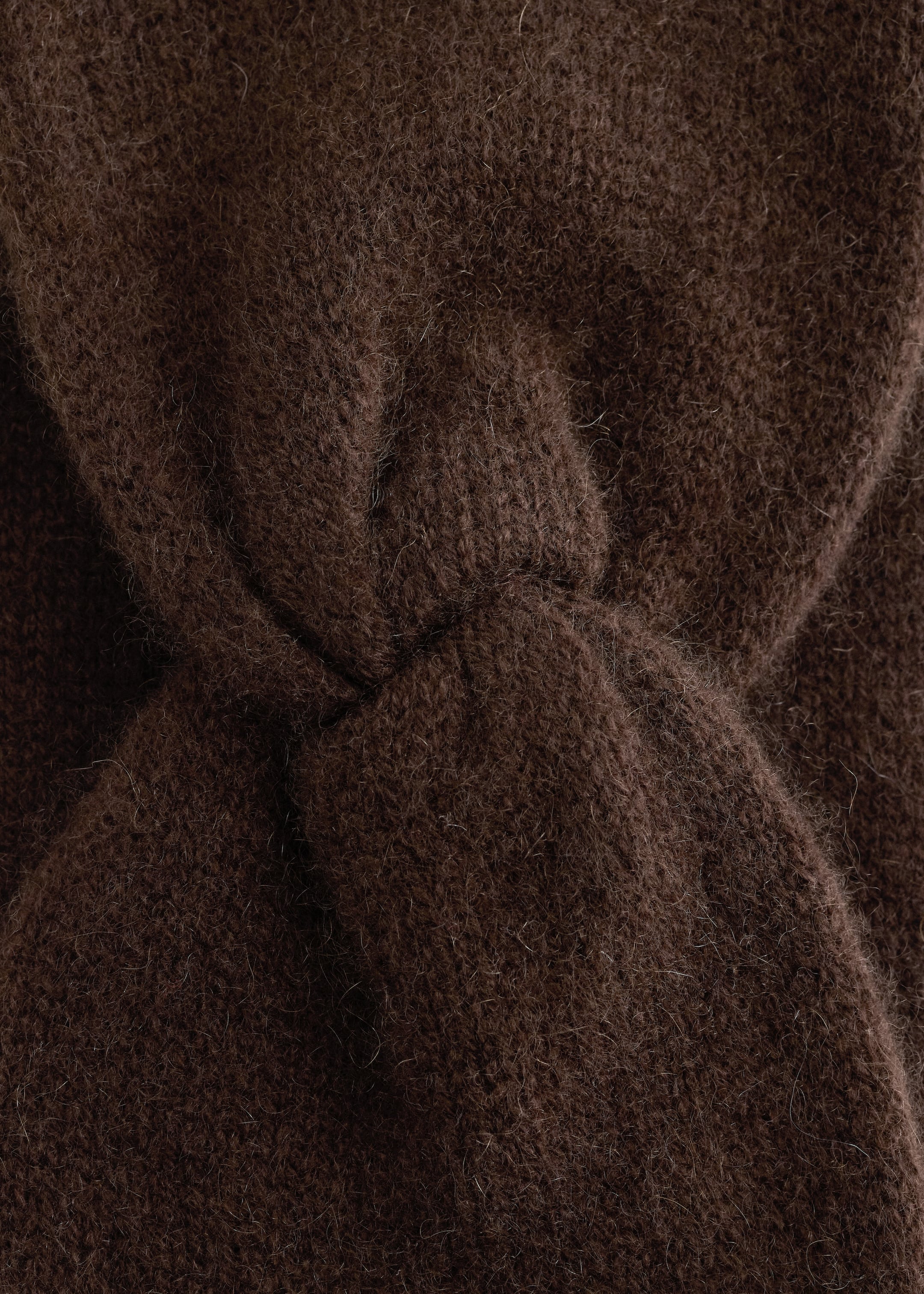 Se større billede: Et brunt strikket pandebånd præsenteres fra sin front, med en fremtrædende central twistknude. Dets brede bånd viser en blød, fnugget tekstur, karakteristisk for cashmere.