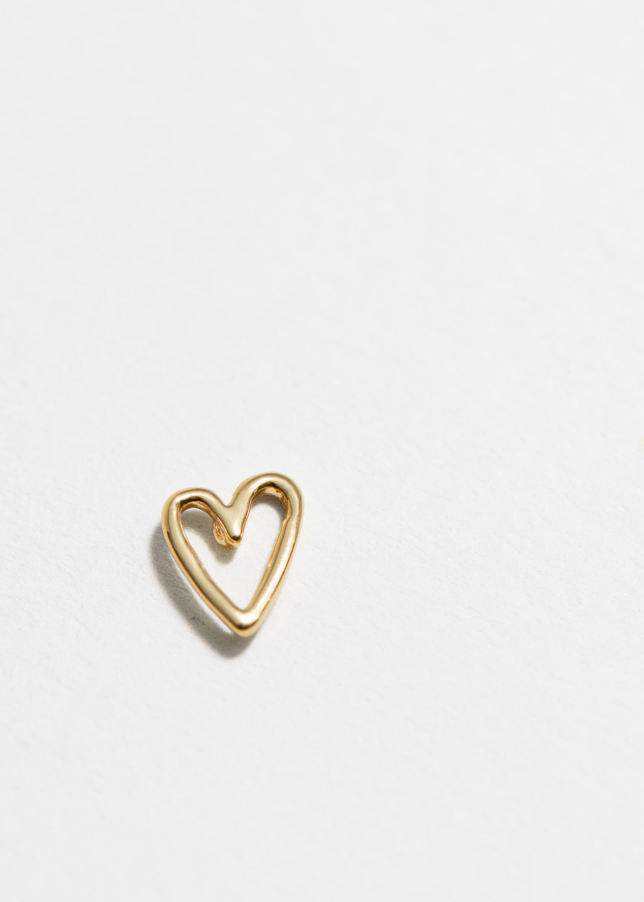 View larger image: A golden heart-shaped charm is lying flat, featuring a smooth, rounded surface and an organic, open design.