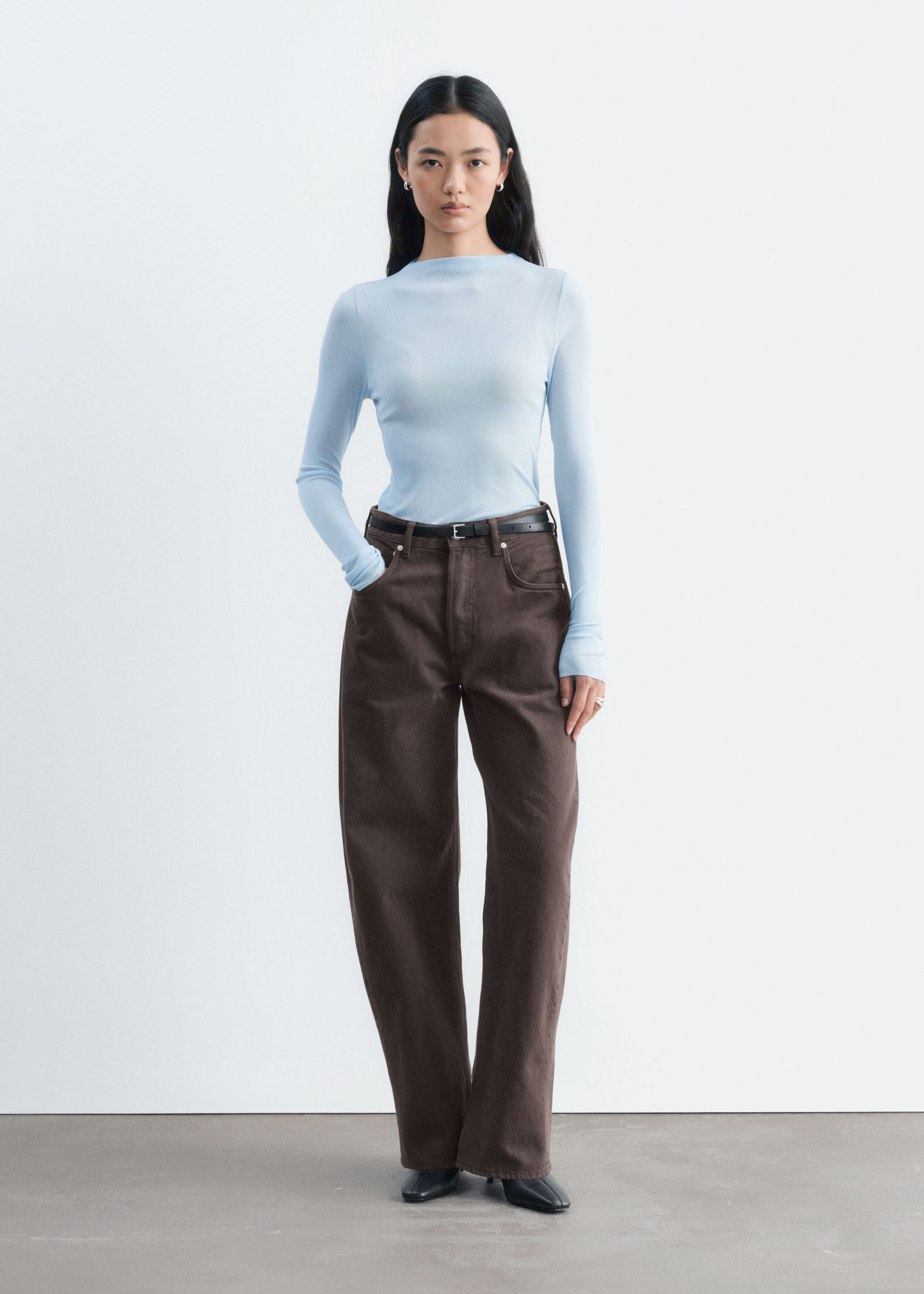 En ljusblå ribbad topp i siden med polokrage och långa ärmar bärs av modellen. Den åtsittande toppen är instoppad i bruna jeans med hög midja och vida ben, stylade med ett svart bälte.