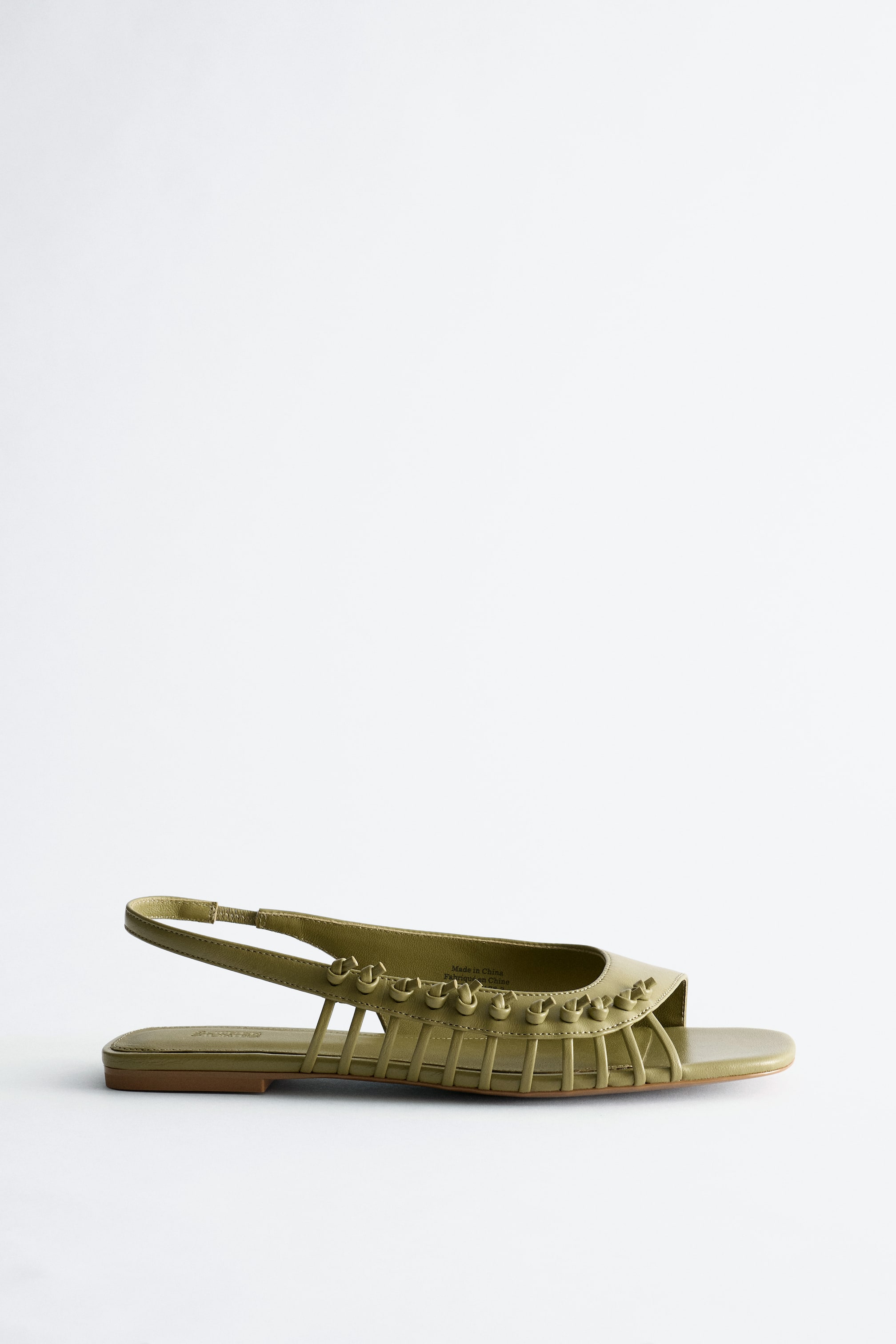 Ver imagem maior: Uma sandália slingback plana em verde oliva é mostrada de um ângulo lateral, apresentando uma ponta quadrada e um design superior intrincado em forma de gaiola com pequenos nós decorativos ao longo do peito do pé.