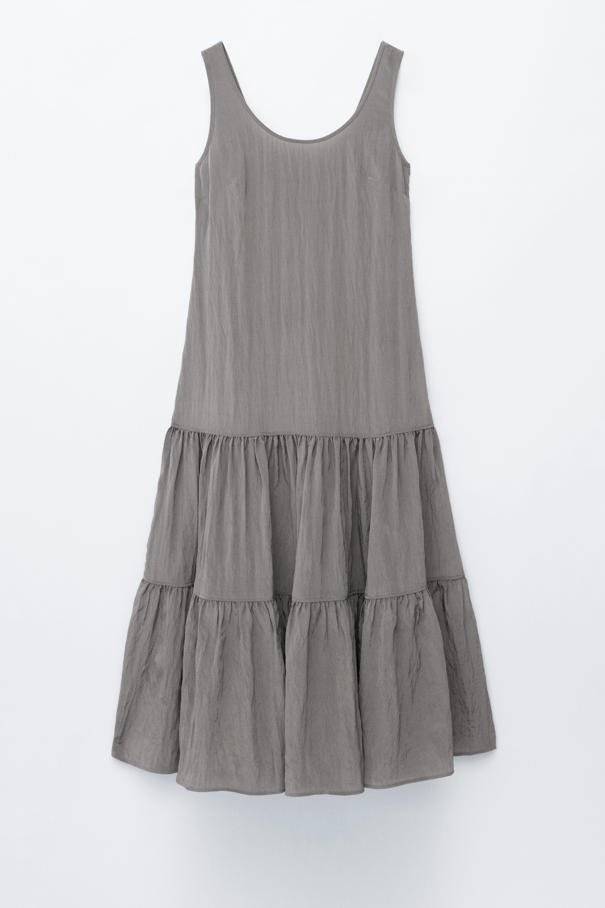 Visa större bild: En grå ärmlös klänning med en rund halsringning och ett texturerat, lätt skrynklat tyg. Kjolen formar tre horisontellt rynkade lager.