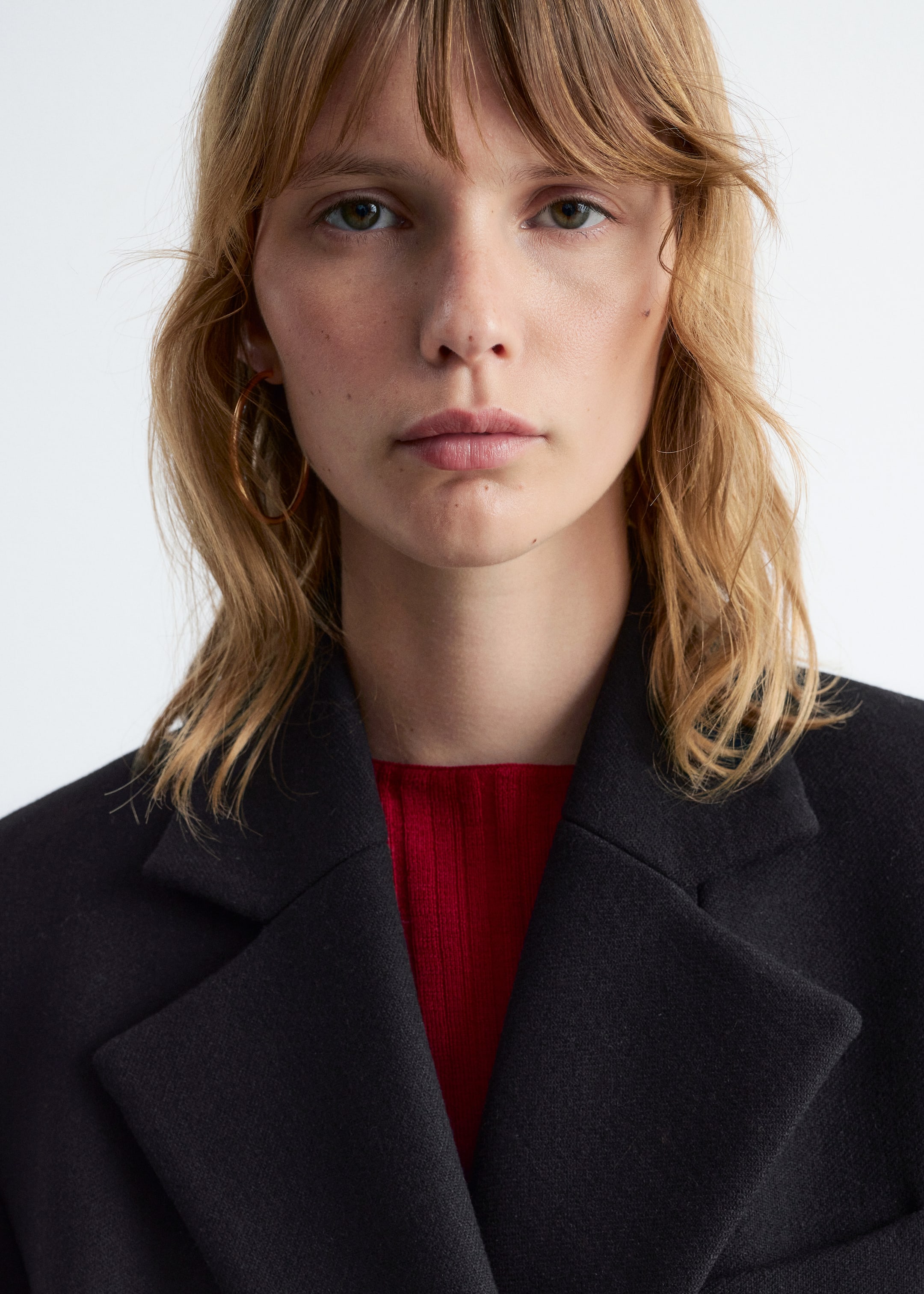 View larger image: A black jacket is being worn, featuring wide, flat notch lapels. A red, ribbed top is visible underneath, layering below the jacket's opening.