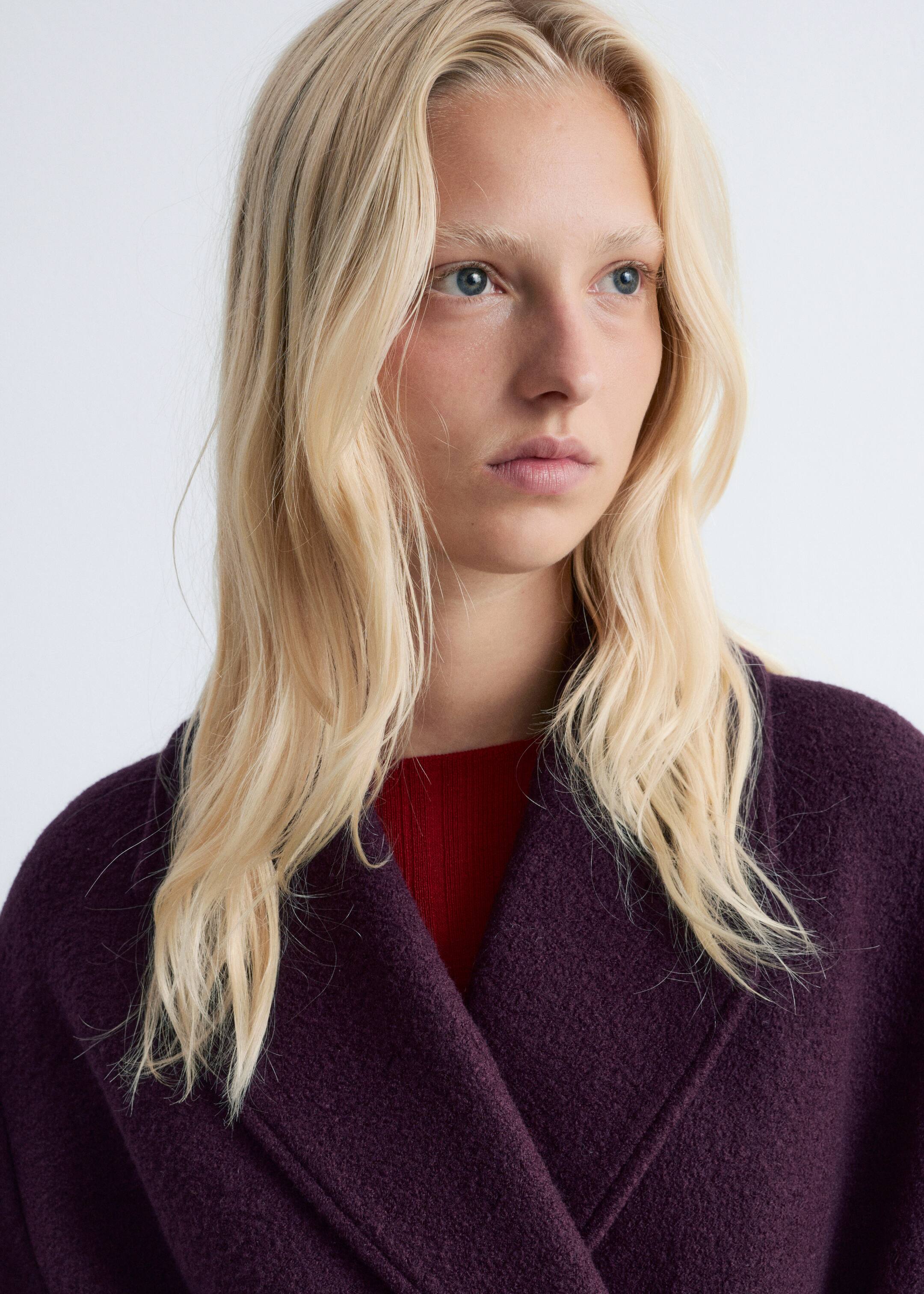 Agrandir l'image: Un manteau texturé d'un violet profond présente de larges revers superposés, porté sur un haut rouge côtelé visible.