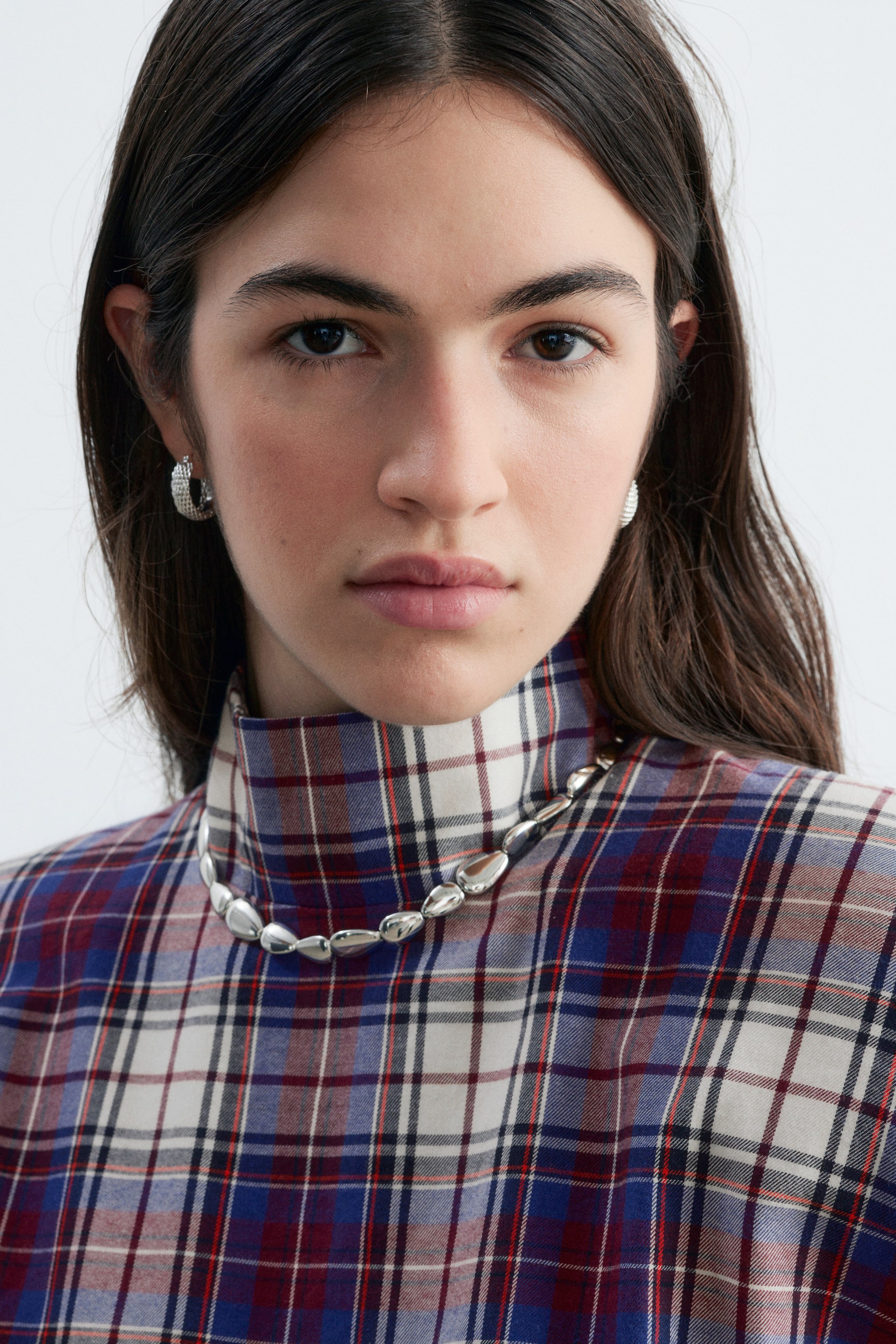 Ver imagen más grande: Un collar de color plateado pulido con cuentas de forma orgánica y bordes suavemente redondeados lo lleva la modelo sobre el cuello alto de un top de cuadro.