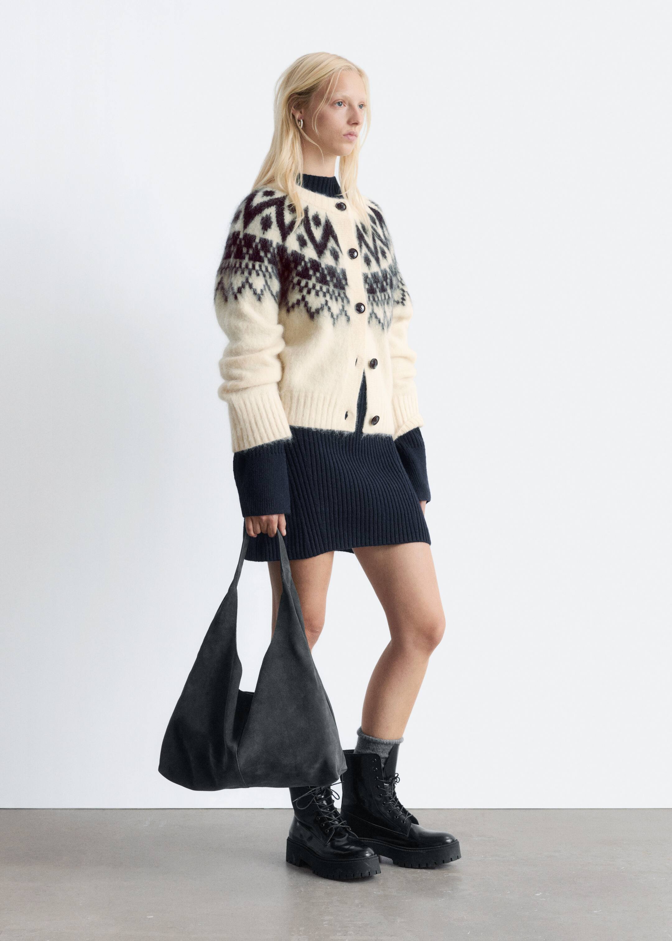 Größeres Bild anzeigen: Eine cremefarbene, flauschige Strickjacke weist ein dunkles Fair-Isle-Muster über der Brust und den oberen Ärmeln auf, das zu einem soliden dunklen unteren Körper und gerippten Bündchen übergeht. Sie präsentiert einen runden Halsausschnitt und eine dunkle Knopfverschluss vorne und ist dreiviertel nach rechts ausgerichtet.