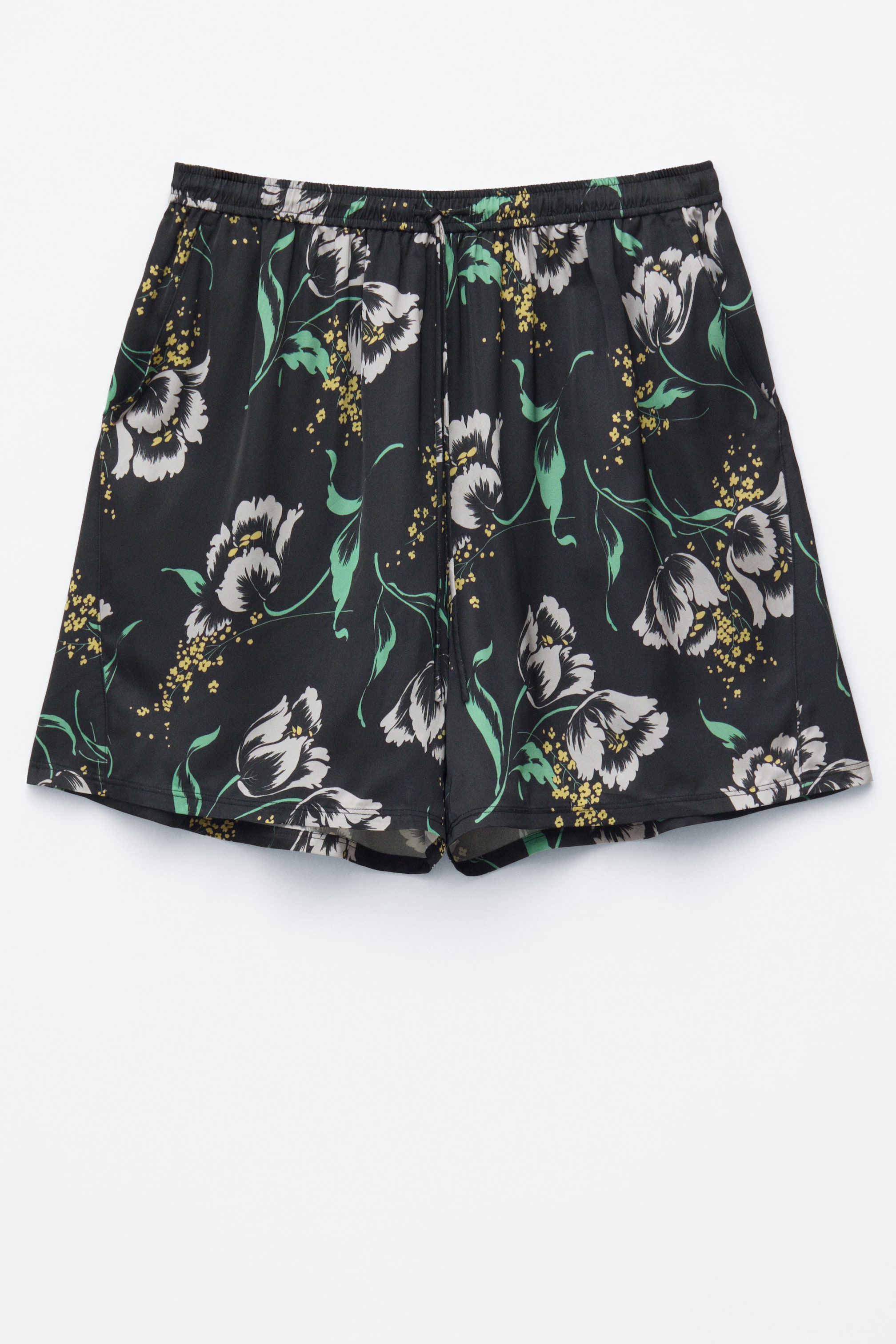 Ver imagen más grande: Los pantalones cortos negros presentan un estampado floral completo de flores blancas y grises, hojas verdes y racimos amarillos. Se muestran desde el frente, destacando una silueta suelta, una cintura elástica con un cordón visible y bolsillos en las costuras laterales.