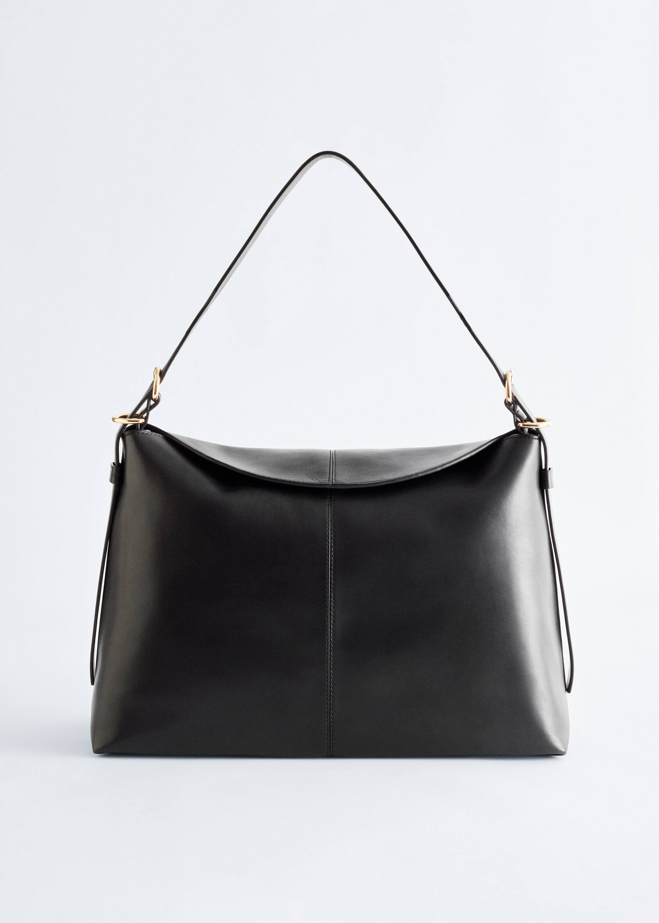 Grösseres Bild ansehen: Eine schwarze Schultertasche aus Leder ist nach VORN ausgerichtet und zeigt ihre elegante, großzügige Form. Eine weiche Klappe schließt mit einer zentralen vertikalen Naht, und eine passende vertikale Naht erscheint auf dem Hauptteil der Tasche. Ein dünner Riemen ist mit silberfarbenen Beschlägen an den Seiten der Tasche befestigt.
