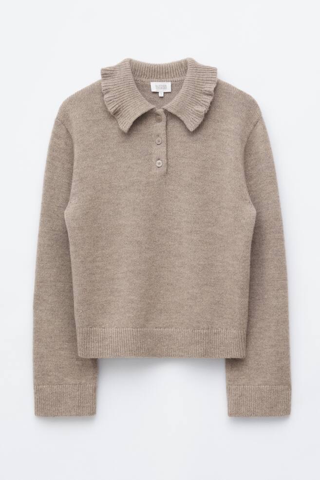 Un jersey beige con cuello con volante estÃ¡ orientado hacia el frente, mostrando un amplio cuello con volante acanalado y una tapeta de tres botones. El jersey de punto de manga larga presenta puÃ±os acanalados y un bajo acanalado a juego. - 1