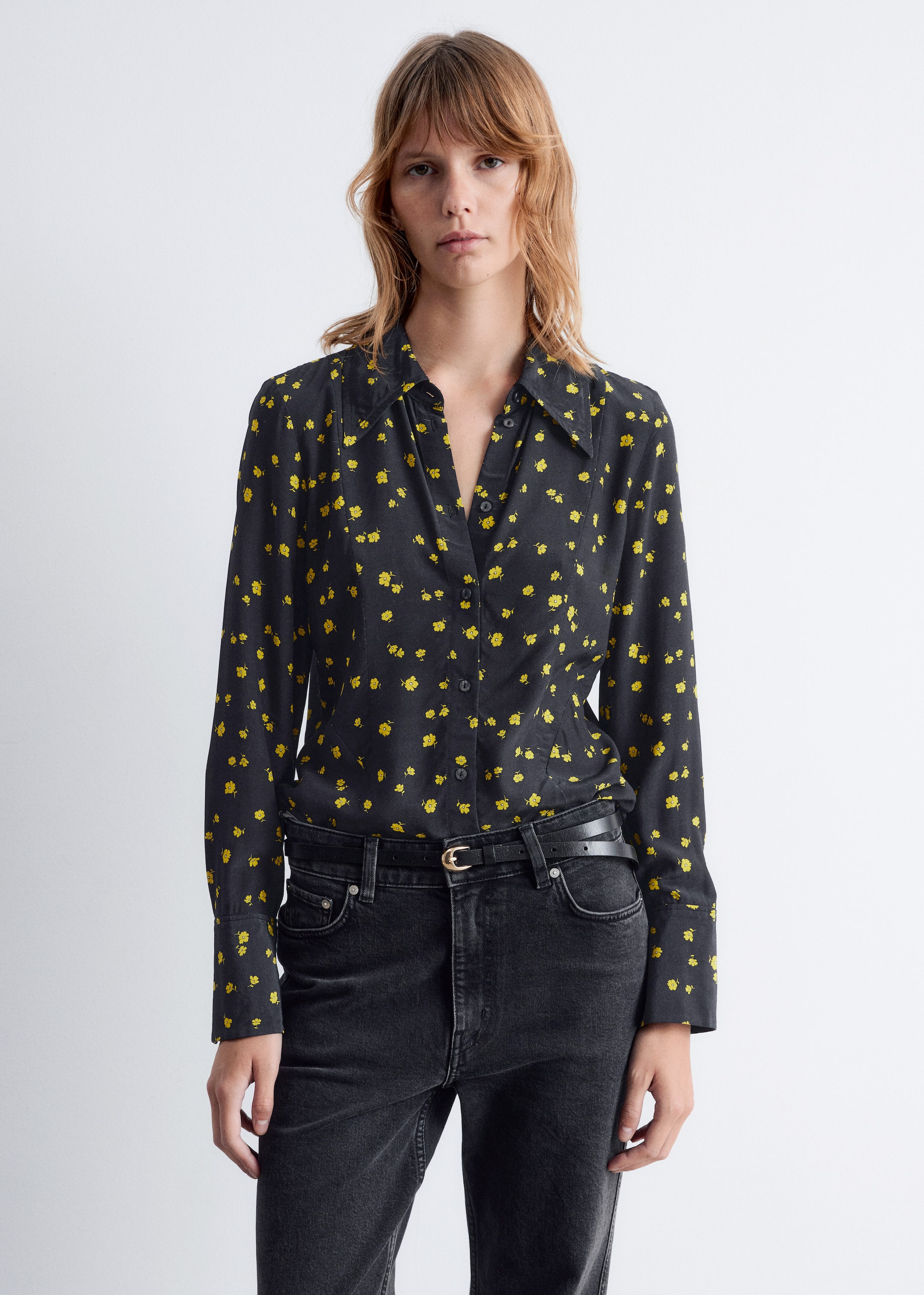 View larger image: A black button-up shirt featuring a yellow floral pattern is being worn. The long-sleeved shirt is presenting a pointed collar and is tucked into a pair of black high-waisted jeans, with a black belt and gold buckle visible at the waist.