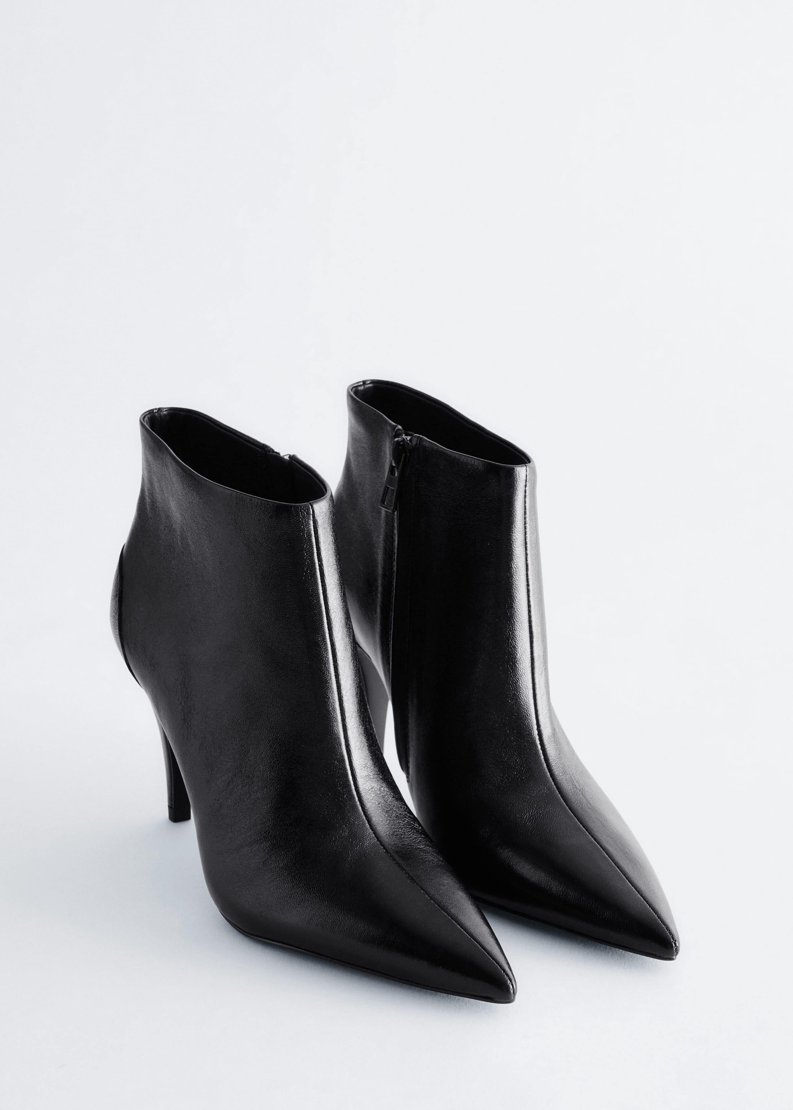 A pair of black leather ankle boots is positioned at a three-quarter angle facing forward, showcasing their pointed toes and high stiletto heels. The boots feature a smooth leather finish with a covered side zip visible on the inner ankle.