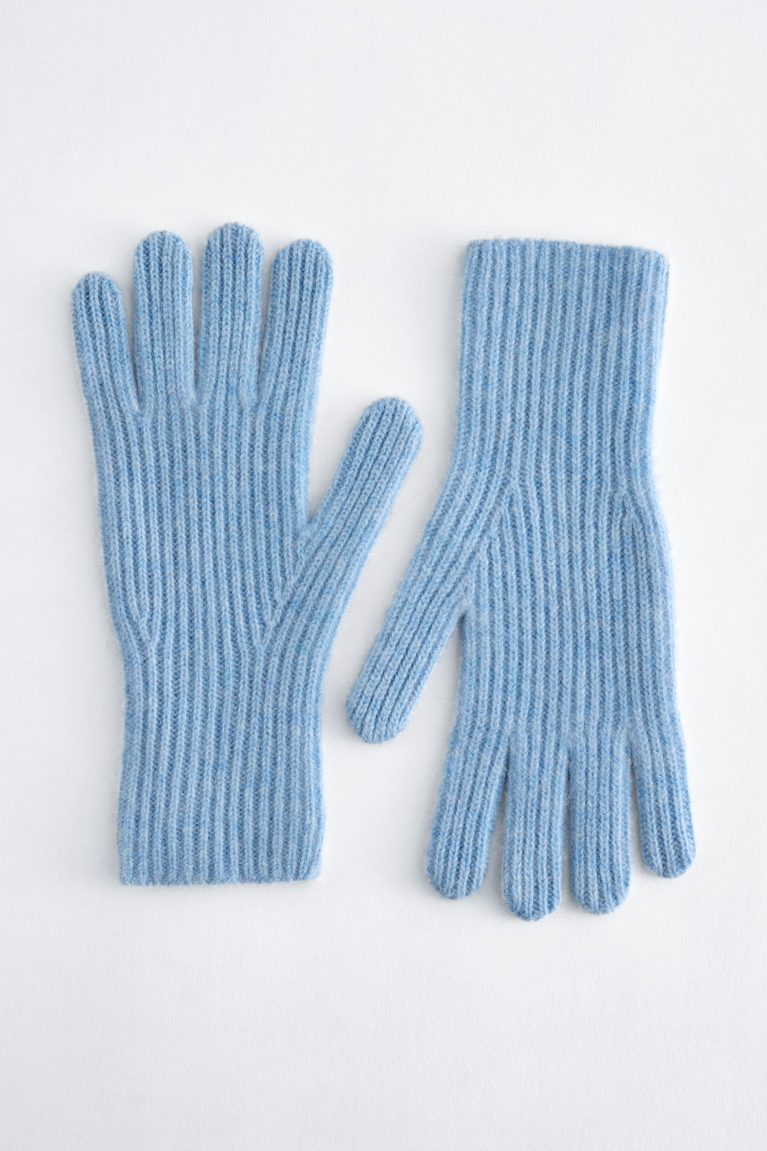 Une paire de gants en cachemire bleu clair est posée à plat, mettant en valeur leur design en maille côtelée texturée. Un gant est orienté vers le haut et lâautre vers le bas, montrant la construction de lâavant et de lâarrière.