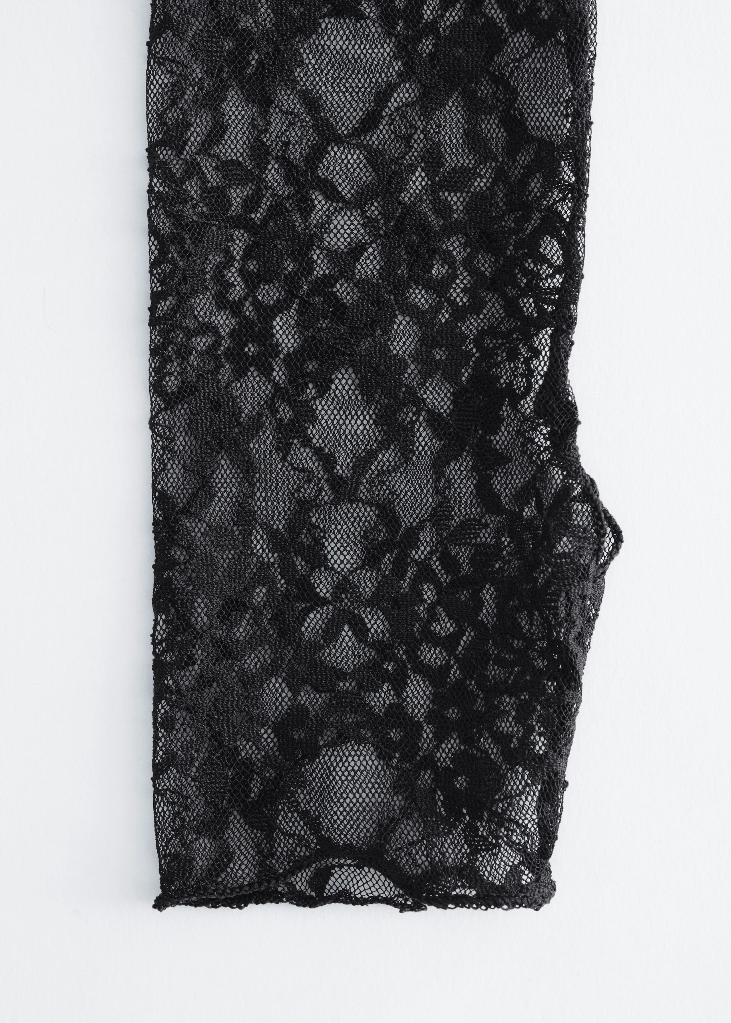A black fingerless glove made from sheer floral lace is laid flat in a front view, showcasing its intricate webbed pattern and a small thumb opening along the side.