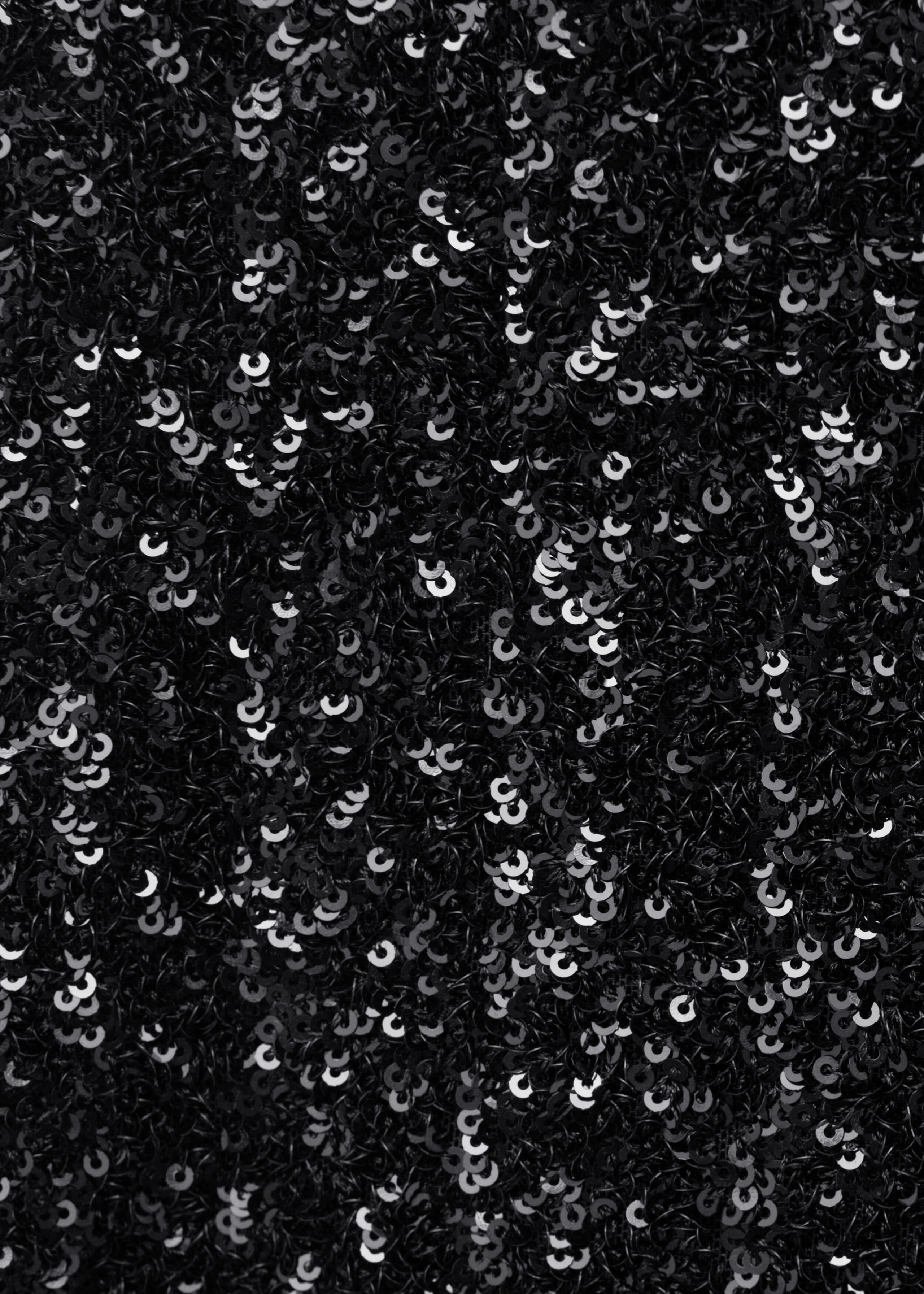 Black sequined fabric is shown in a close-up view, featuring a dense arrangement of small, glossy sequins that catch the light and create shimmering metallic highlights.