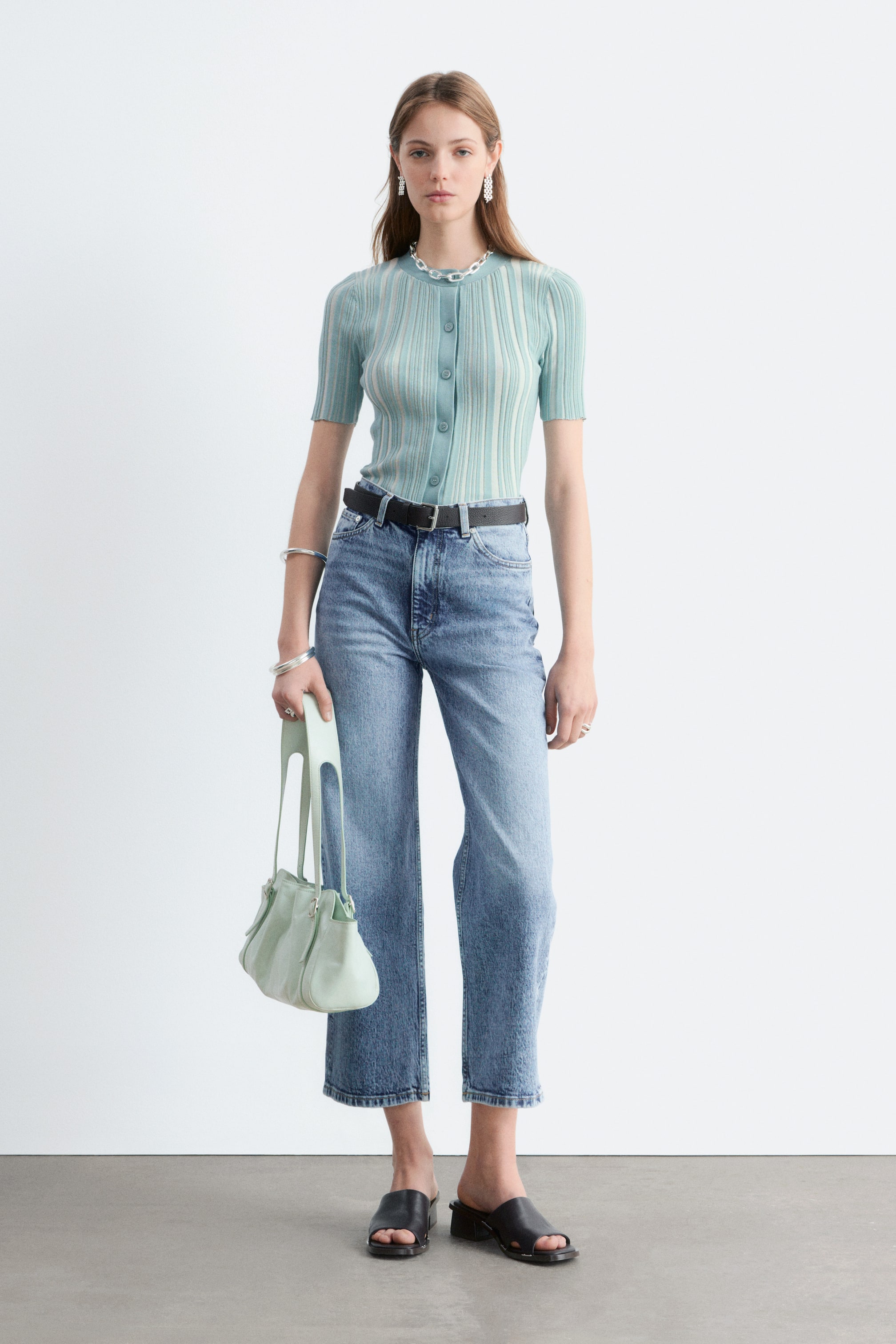 Größeres Bild anzeigen: Blaue Denim-Jeans mit hoher Taille und sichtbarem Knopfverschluss, klassischem 5-Taschen-Design und verkürzten, weiten Beinen werden vom Model getragen. Die Jeans sind knöchellang, und ein schwarzer Gürtel ist durch die Gürtelschlaufen gezogen.