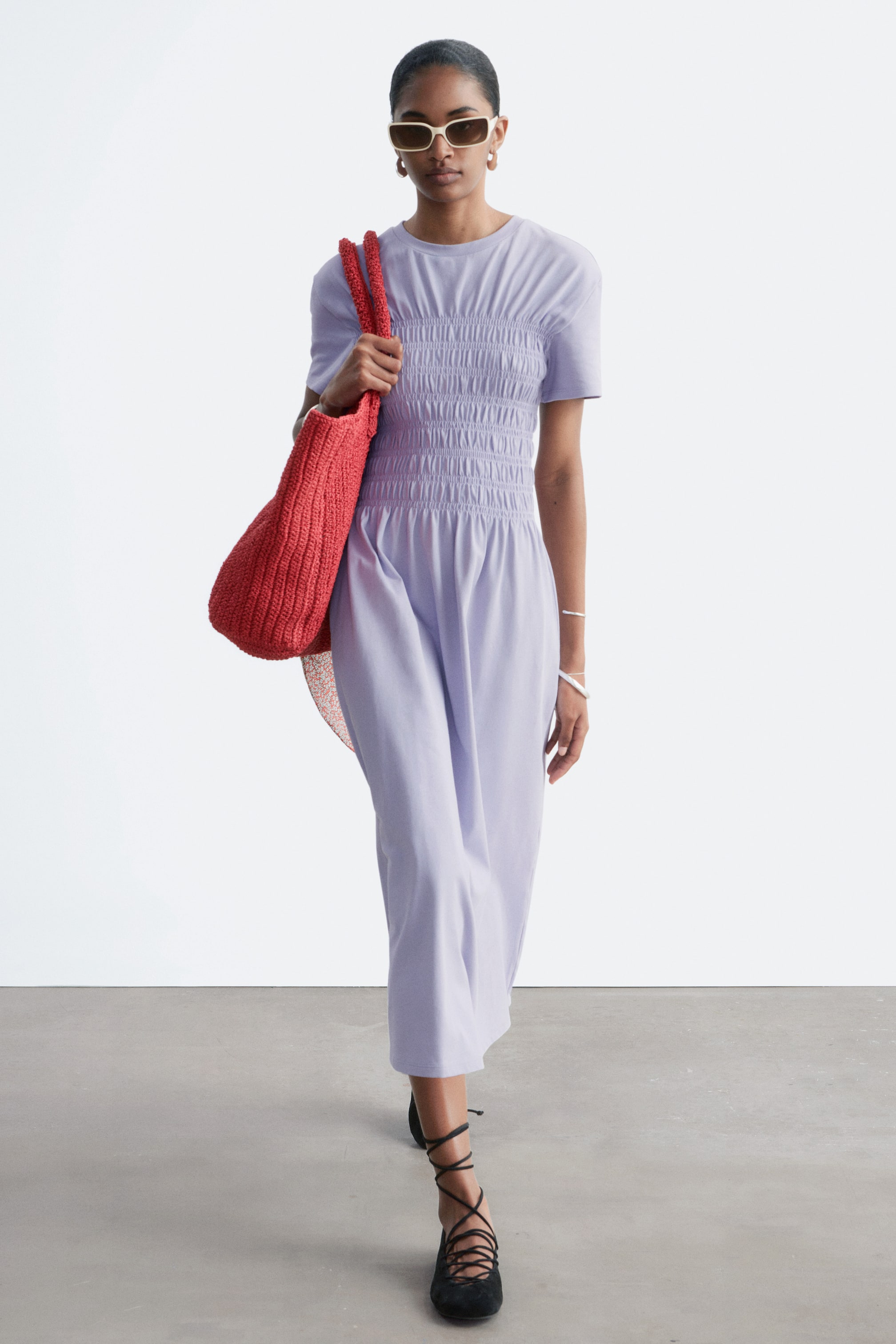 Προβολή μεγαλύτερης εικόνας: Το ανοιχτό μοβ φόρεμα διαθέτει κοντά μανίκια και στρογγυλή λαιμόκοψη. Το μπούστο του παρουσιάζει περίτεχνη σούρα, ενώ η αέρινη φούστα σε μήκος μίντι εκτείνεται μέχρι τη μέση της γάμπας.