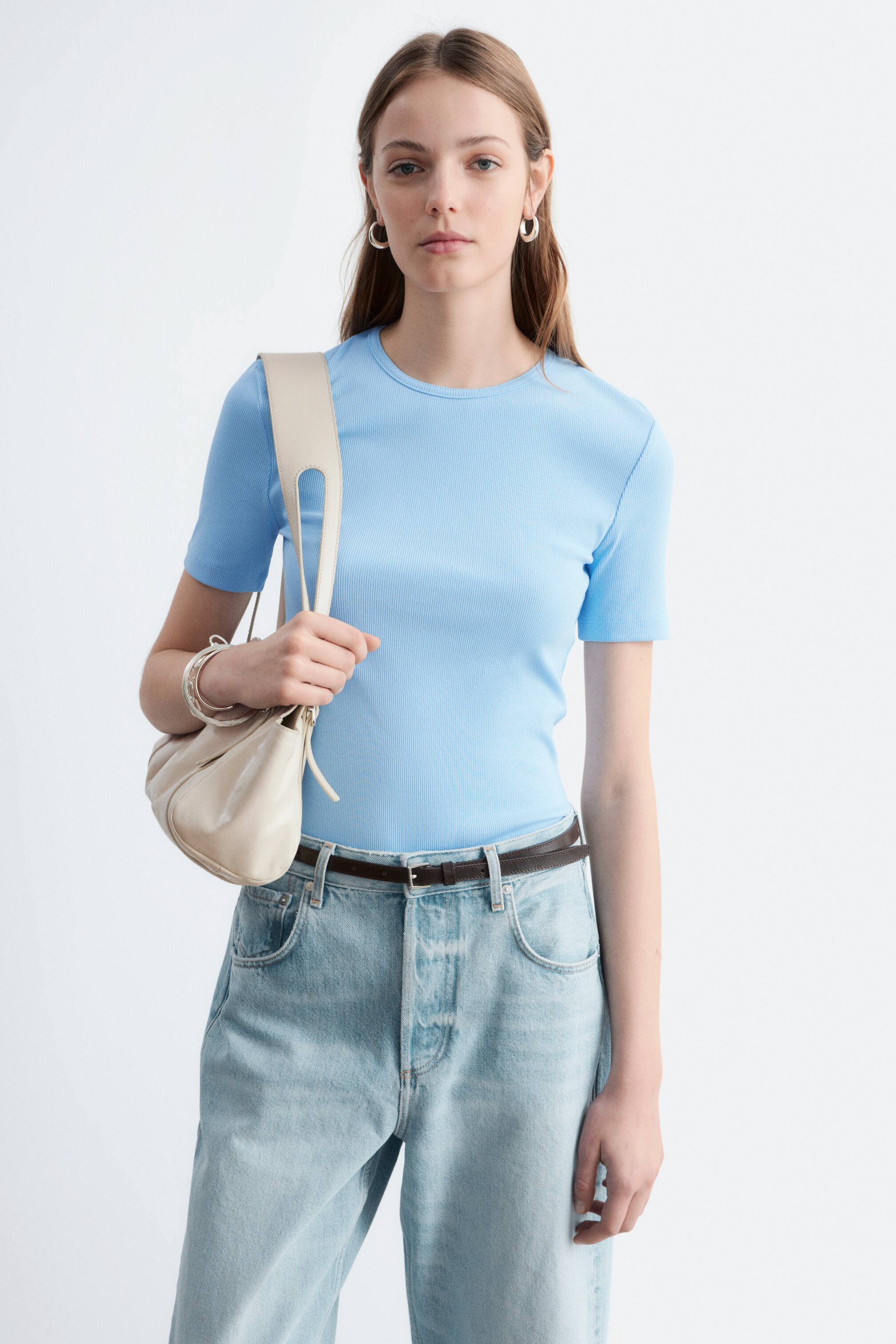 View larger image: A light blue ribbed T-shirt featuring short sleeves and a crew neck, designed to fit closely to the body. It is styled tucked into light-wash jeans.