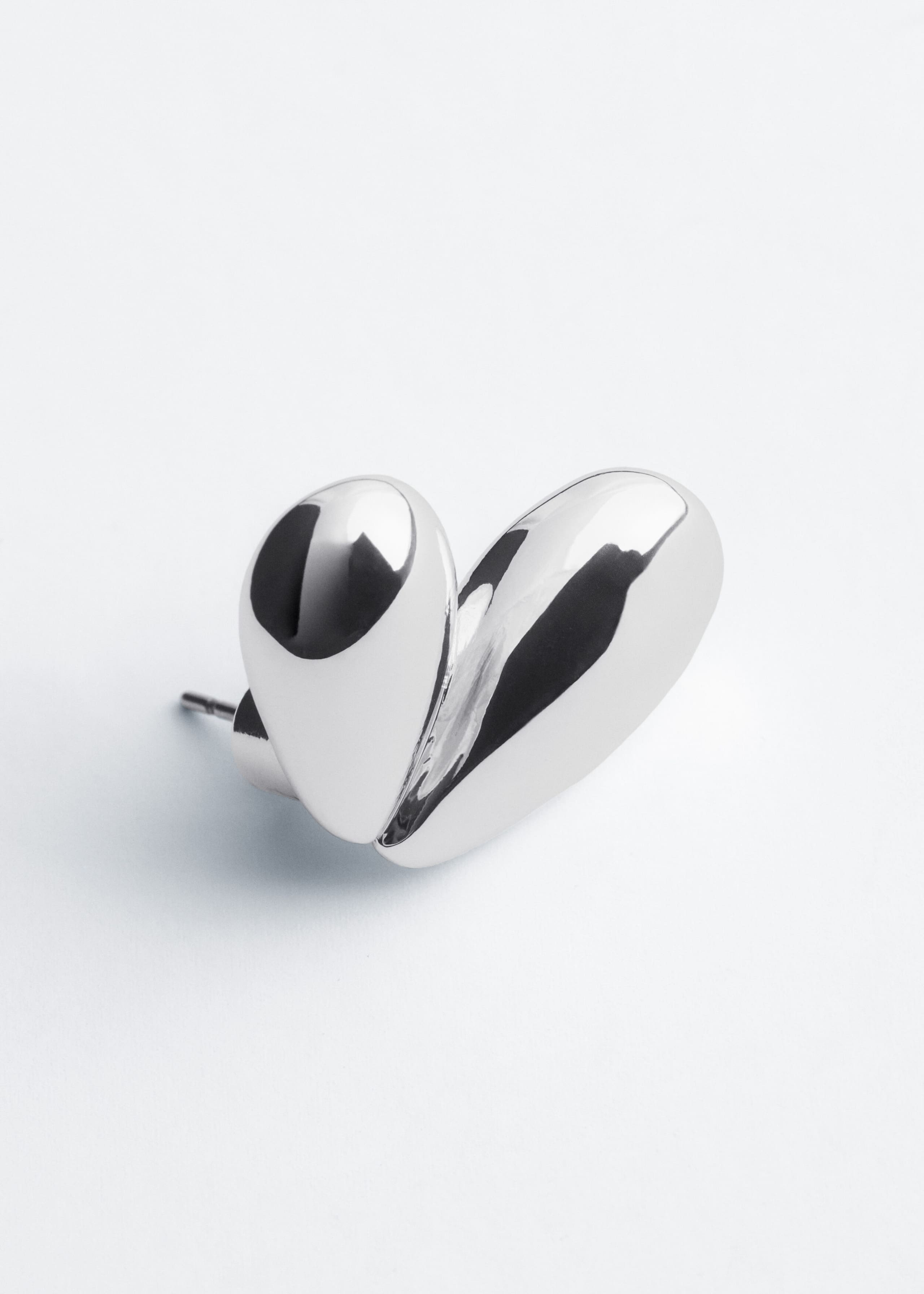 A polished silver-toned stud earring is shown from a three-quarter front angle, highlighting its sculptural, organic design resembling a stylised heart with two bulbous, highly reflective lobes. A post and clasp backing are visible extending from the left side of the smooth metallic piece.