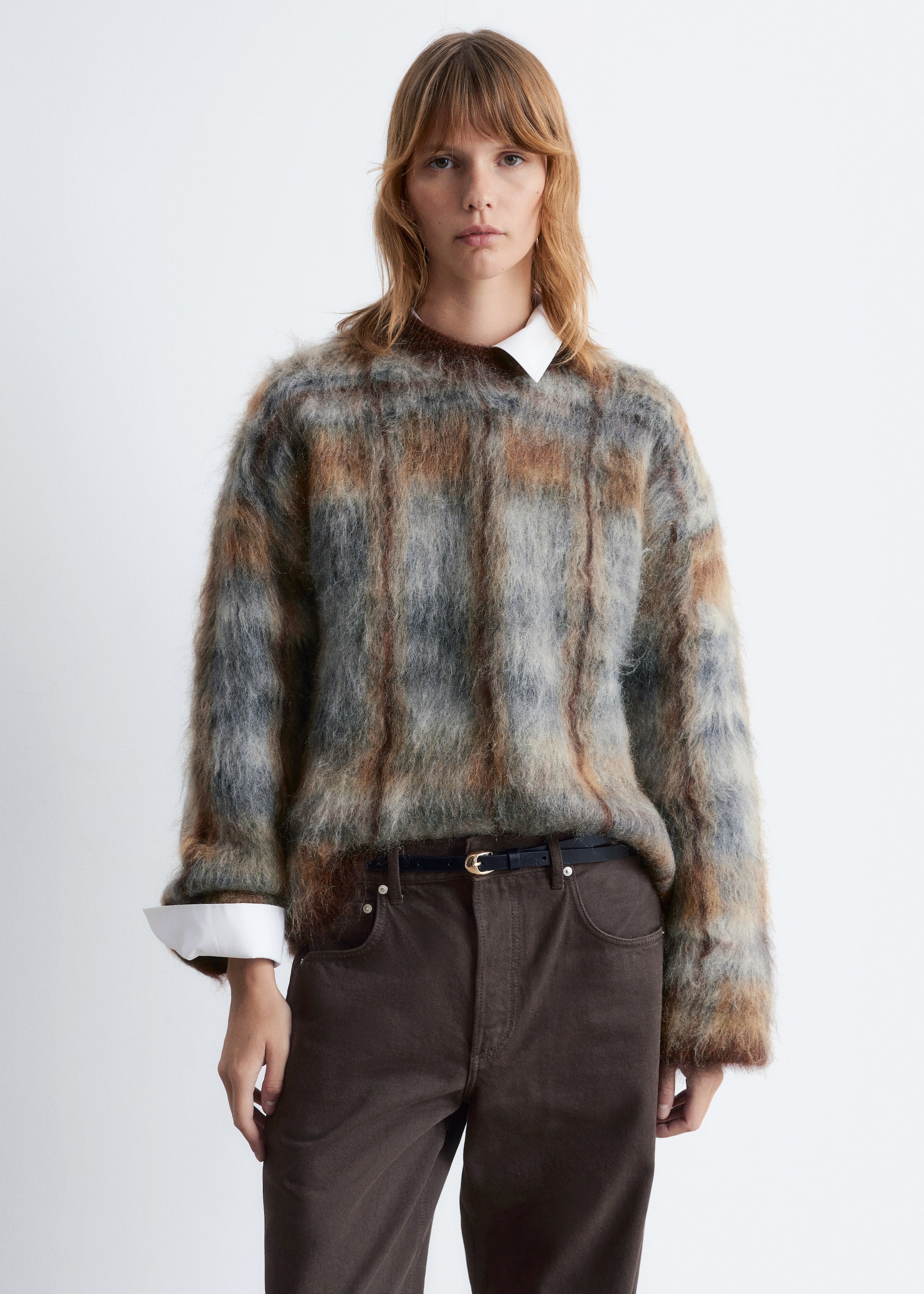 Größeres Bild anzeigen: Ein langärmeliger Pullover, der ein flauschiges, mehrfarbiges Strickmuster in Brauntönen, Grau und Blau aufweist, wird von einem Model getragen. Der locker sitzende Pullover ist über einem weißen Hemd mit Kragen geschichtet, wobei der Kragen des Hemdes am Hals und die Manschetten an den Handgelenken sichtbar sind.