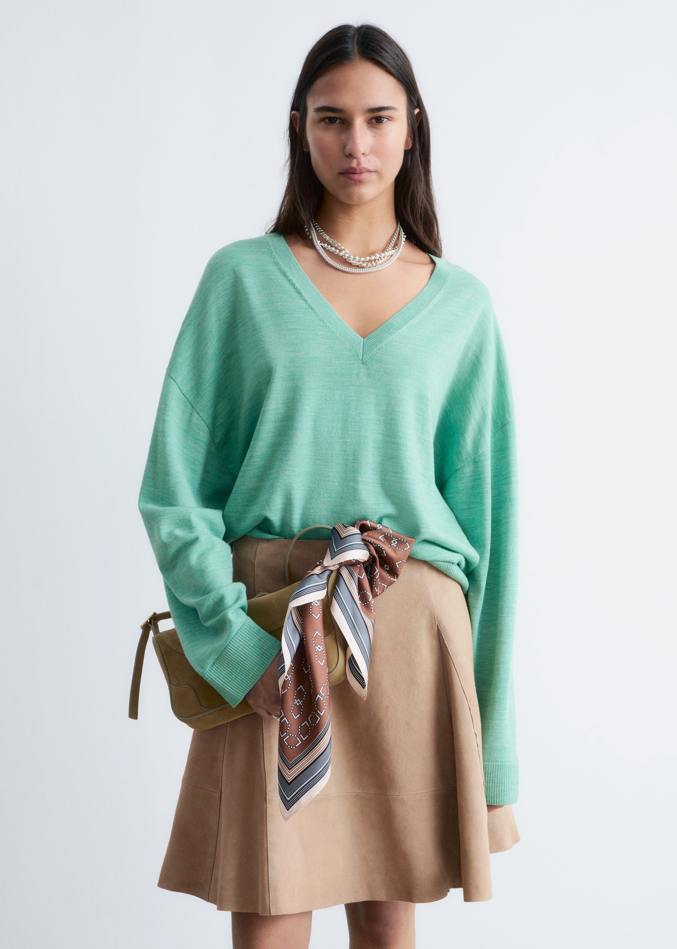 Προβολή μεγαλύτερης εικόνας: "Ένα πουλόβερ σε χρώμα μέντας με V-λαιμόκοψη διαθέτει χαλαρή εφαρμογή με χαμηλωμένους ώμους, μακριά μανίκια, ριμπ μανσέτες και ριμπ στρίφωμα. Εμφανίζει υφή από λεπτή πλέξη και είναι συνδυασμένο με μια φούστα σε χρώμα ταμπά."