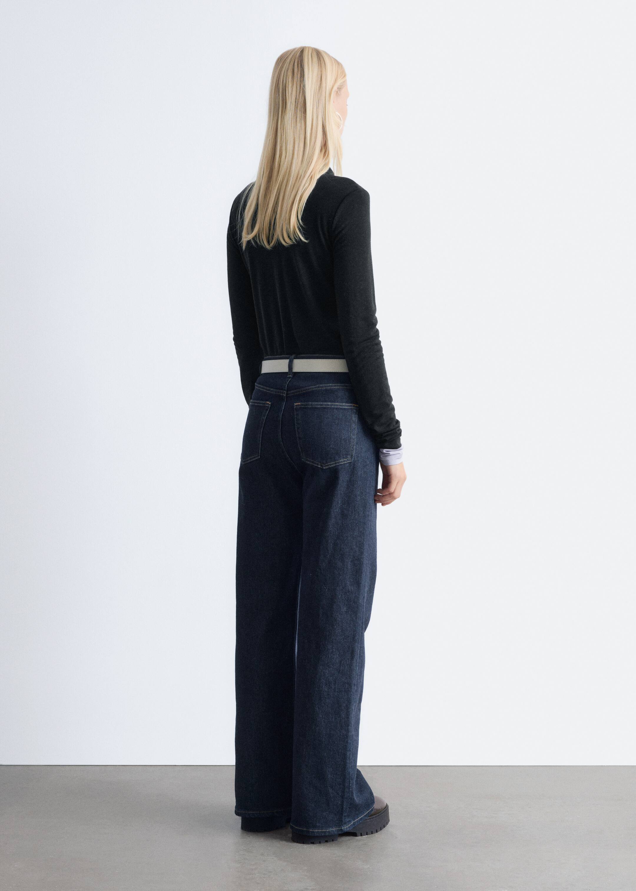 Agrandir l'image: Un haut sombre à manches longues est porté, superposé à une chemise plus claire avec des poignets visibles, et assorti à un jean large à délavage foncé, vu de dos. Une ceinture de couleur claire est passée dans les passants du jean.
